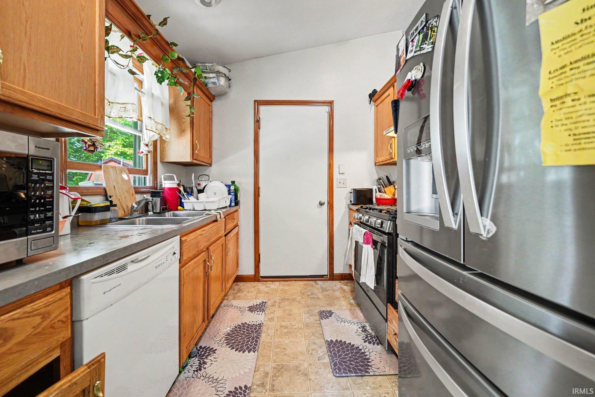 Kitchen featuring wood-finish cabinetry, solid surface countertops, a stainless steel refrigerator, and a built-in dishwasher