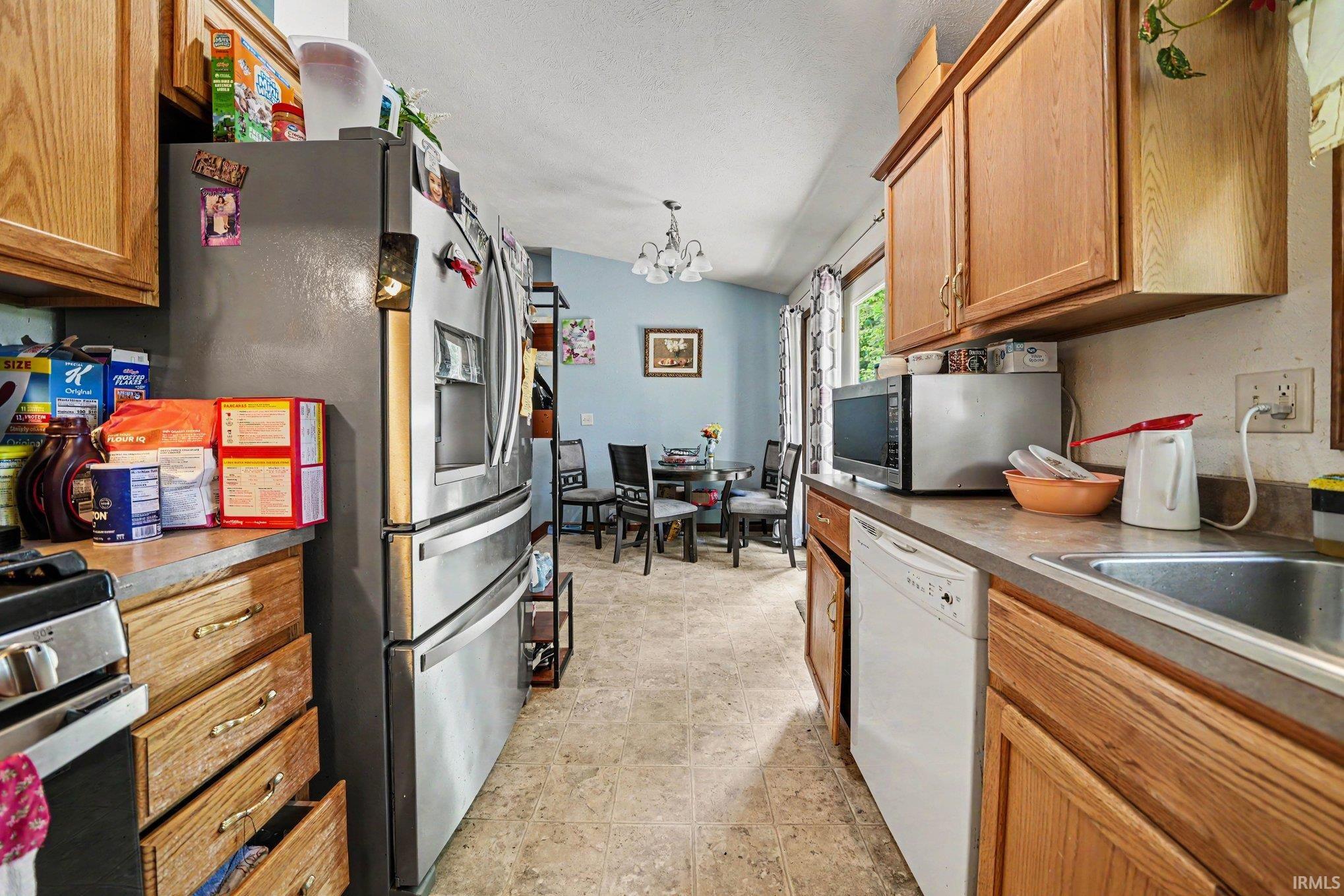 Kitchen featuring wood cabinetry, stainless steel refrigerator, integrated dishwasher, and a dining area beyond