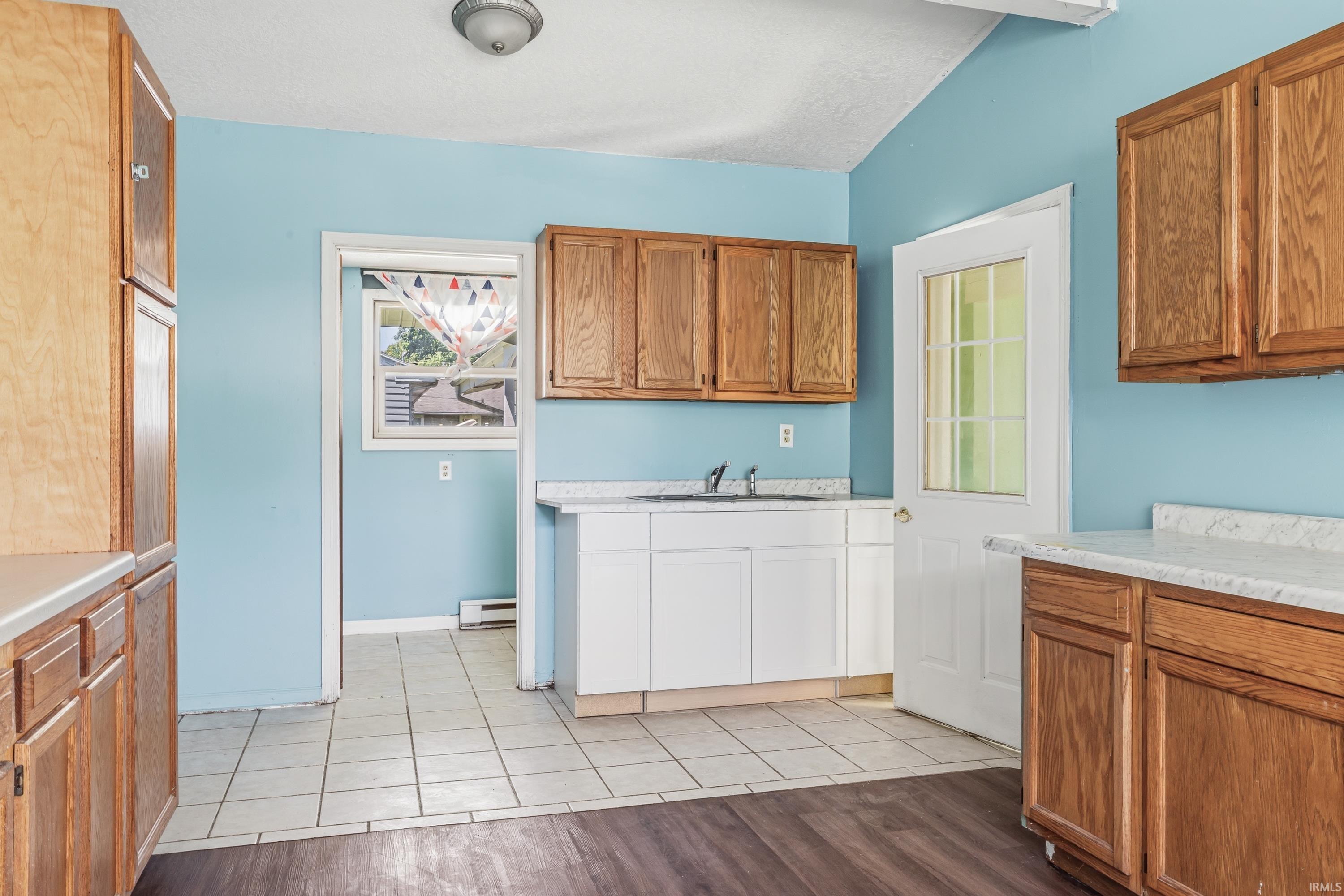 Kitchen featuring a vaulted ceiling with exposed beam, wood-finish cabinetry, white countertops, and a white paneled door with glass inserts