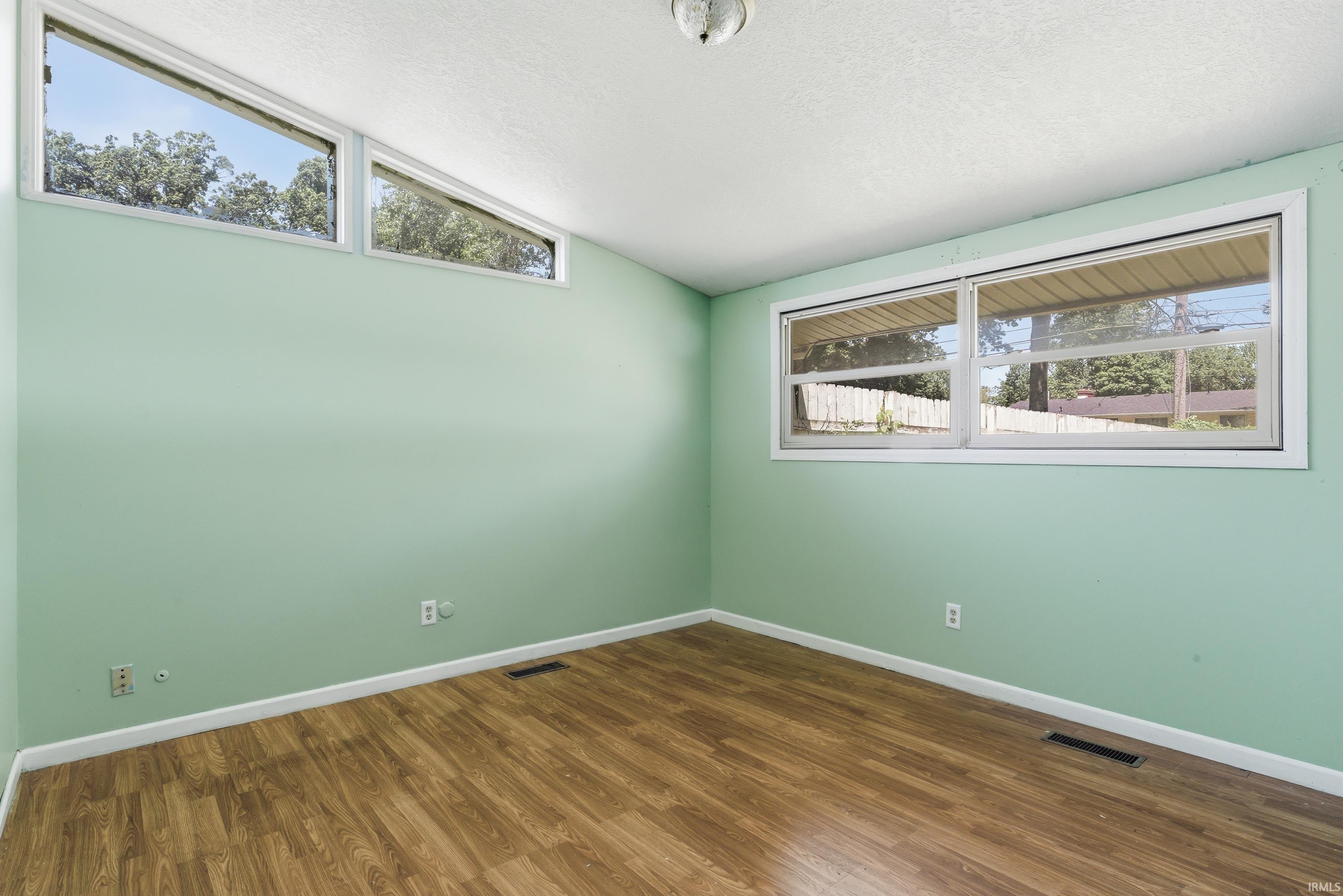 Spacious room featuring wood-finish flooring, light green walls, and white trim