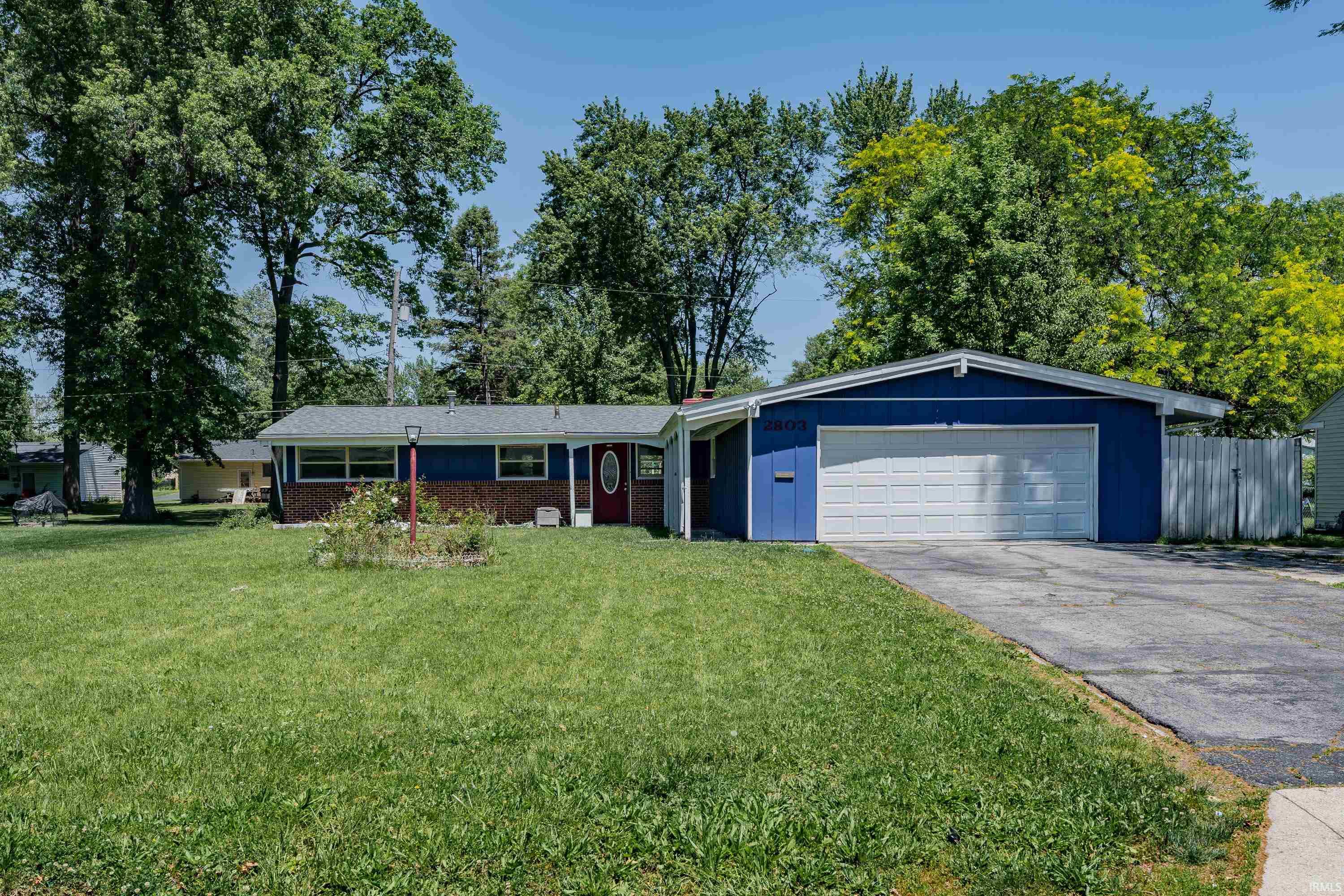 Ranch-style residence featuring a prominent two-car garage, partial brick exterior, and a red entry door