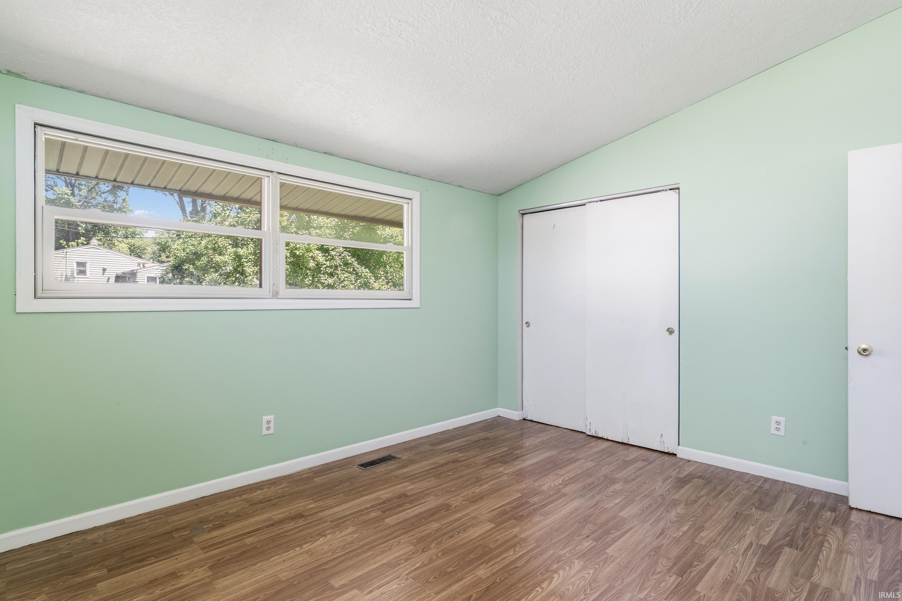 Room featuring wood-finish flooring, a double-pane window, and sliding closet doors