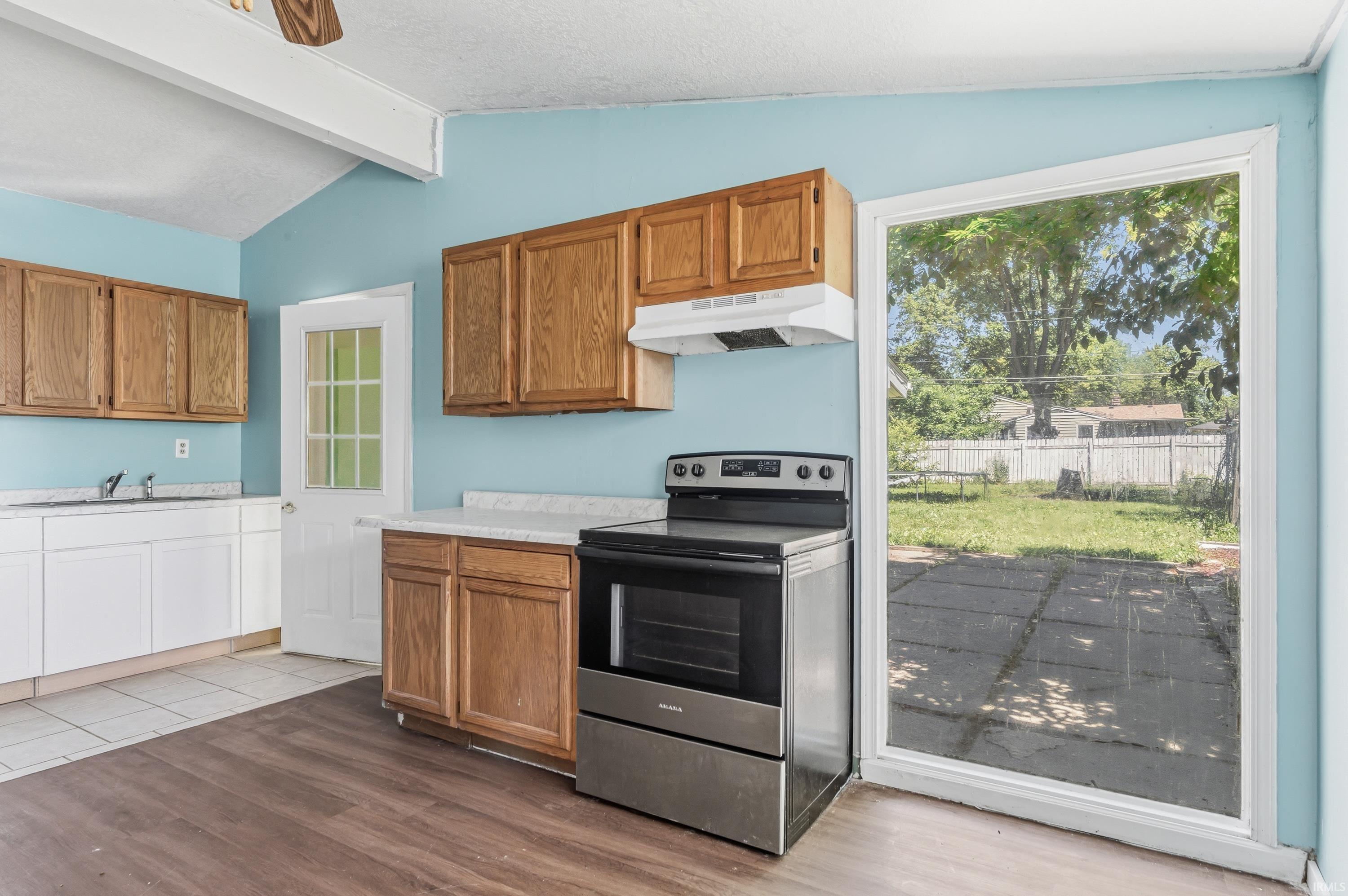 Kitchen featuring wood-finish flooring, two-tone cabinetry, white countertops, and a stainless steel range with overhead ventilation