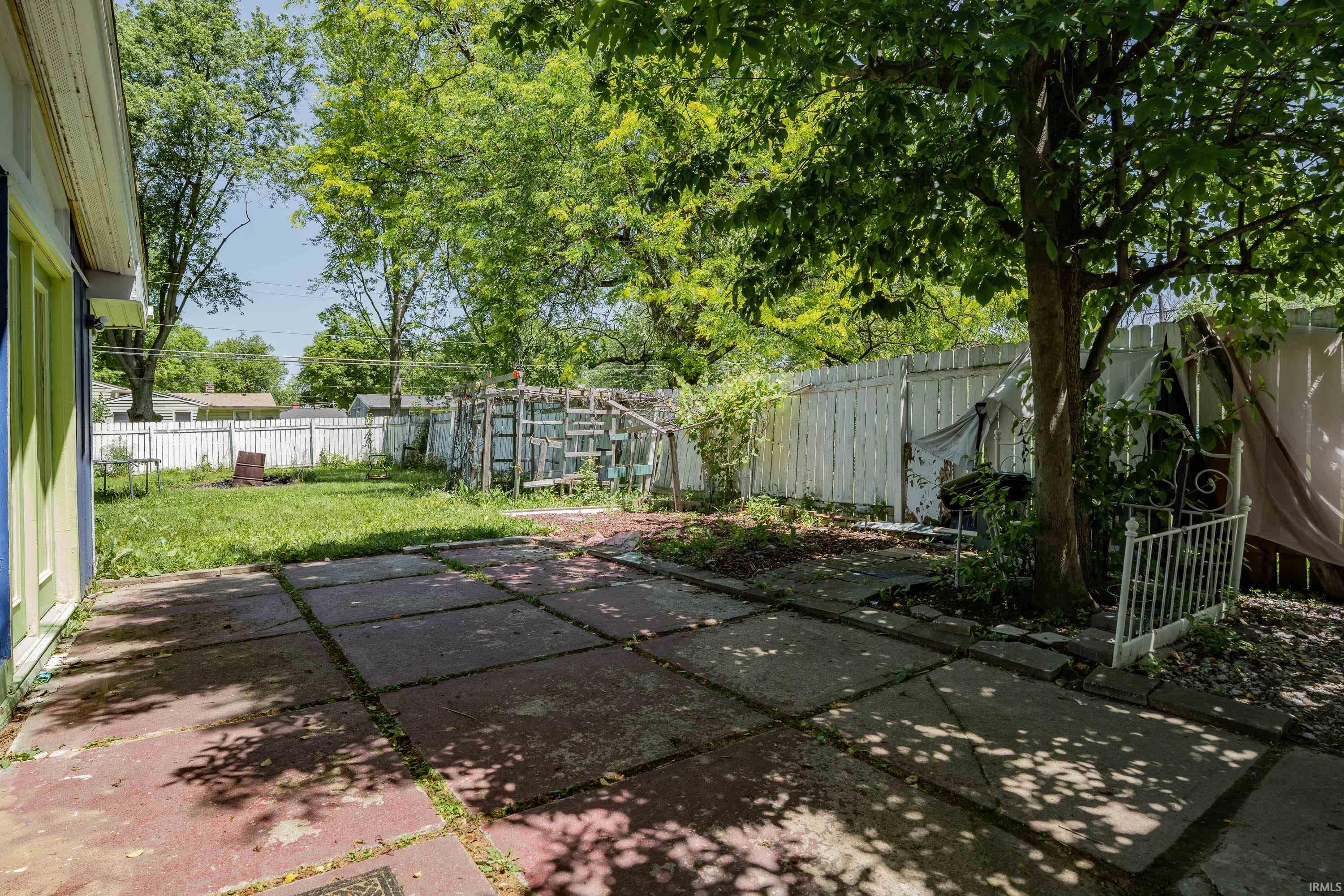 Rear yard featuring a concrete patio, established trees, and a perimeter fence