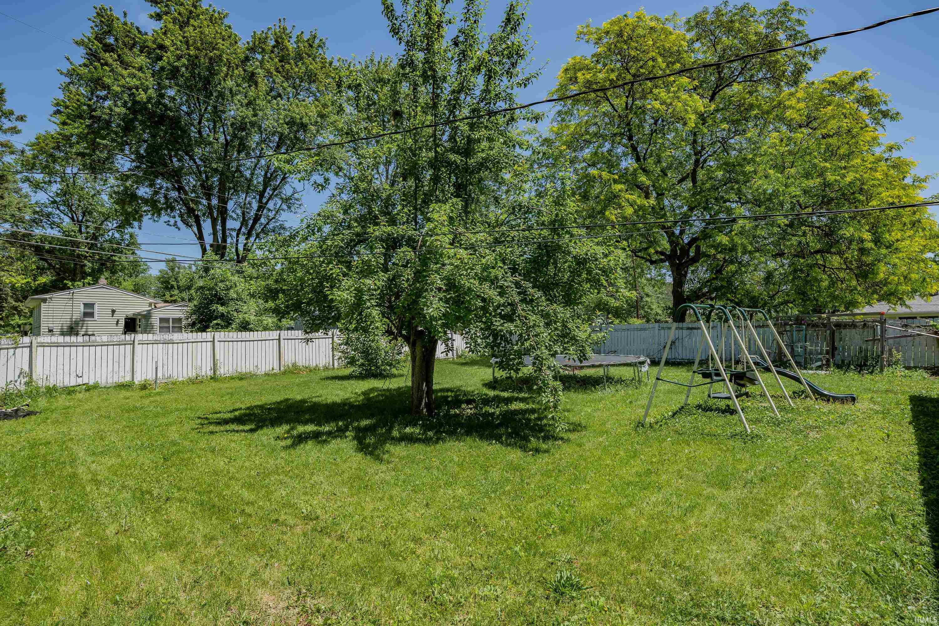 Spacious backyard featuring a lush lawn, mature trees, and a white picket fence