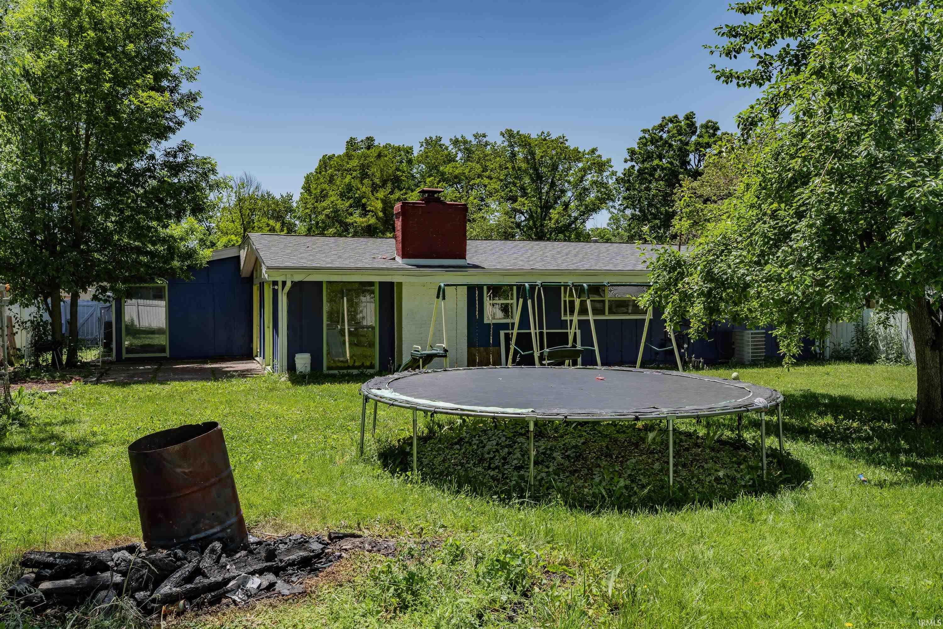 Expansive backyard featuring a green lawn, mature trees, and a detached structure with a blue exterior