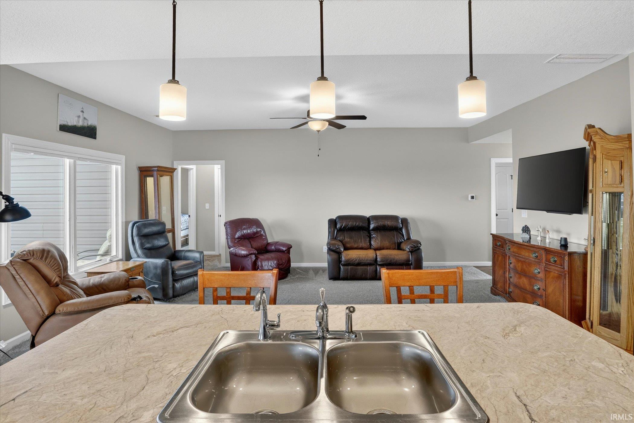 Expansive open-concept living area featuring a kitchen island with a double basin stainless steel sink and a light-toned countertop
