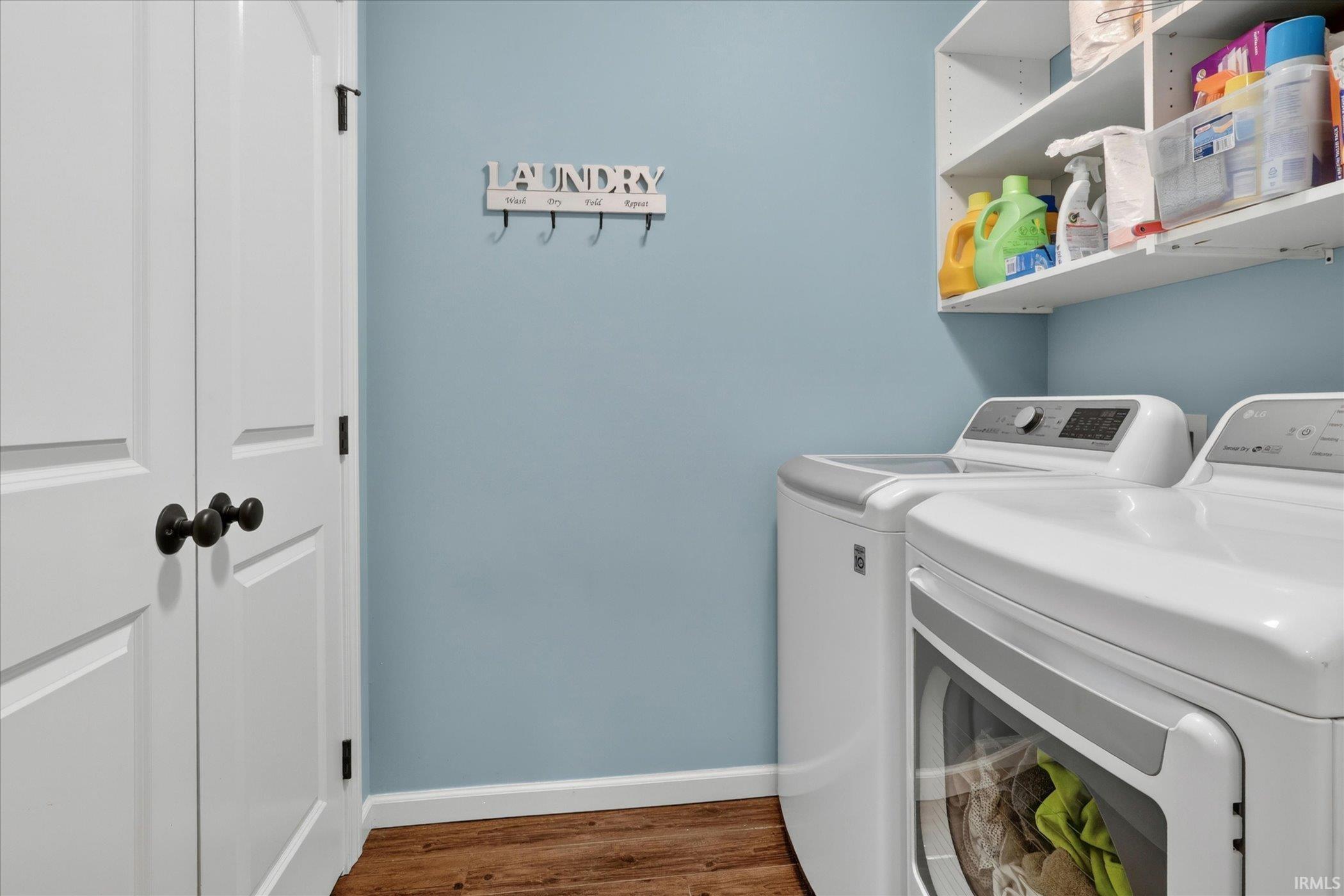 Dedicated laundry area featuring white appliances, a light blue wall, wood-finish flooring, and white built-in shelving