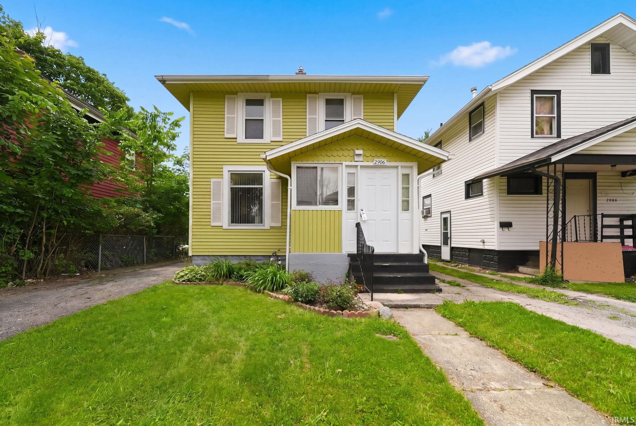 Two-story residence featuring light yellow siding and white window shutters