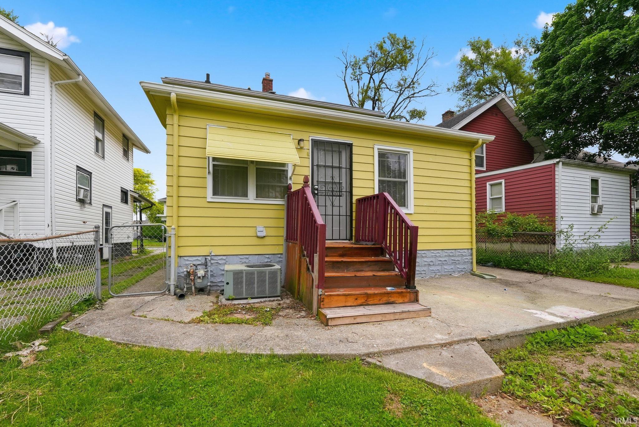 Yellow siding exterior with a concrete patio, wooden steps, and an air conditioning unit