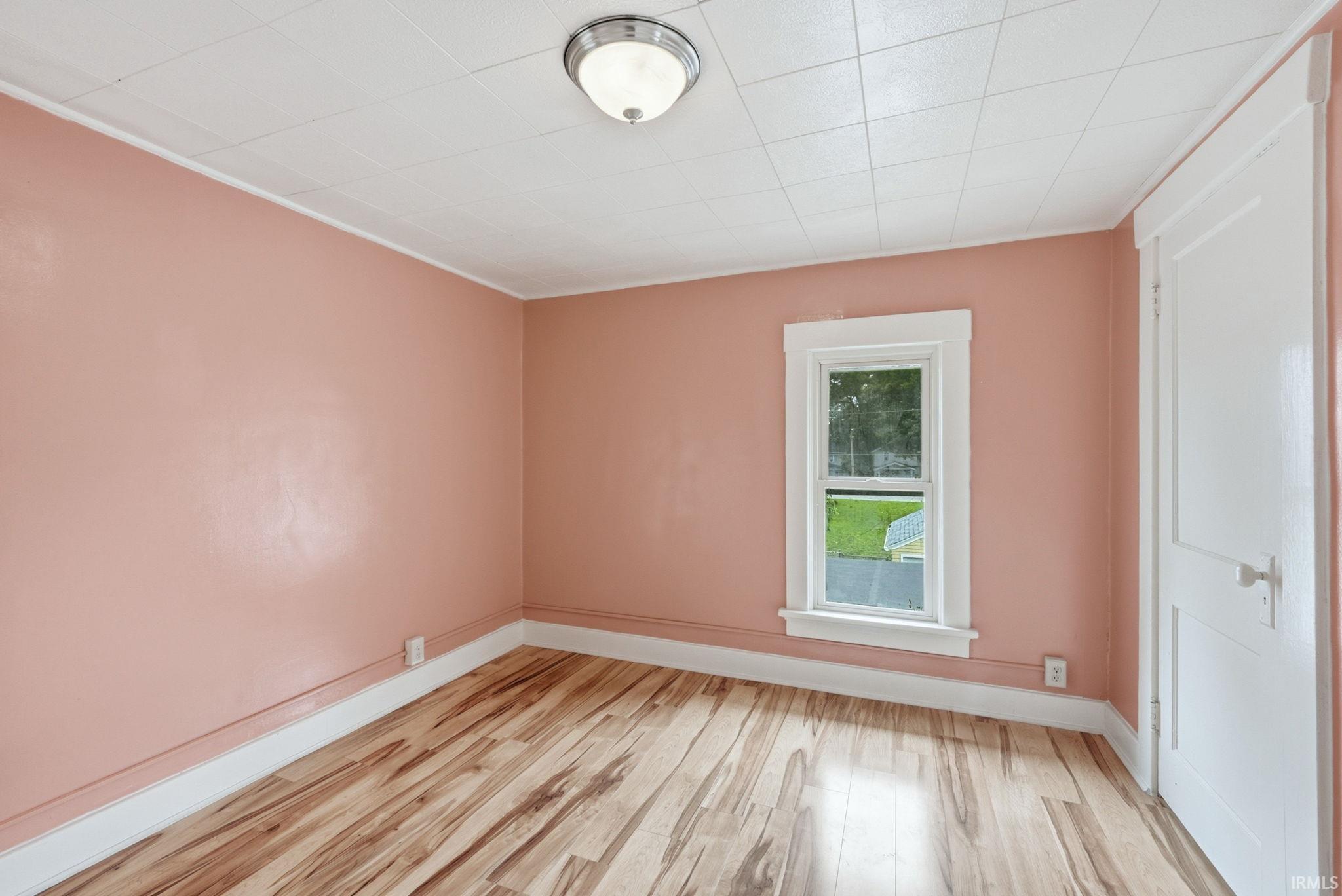 Room featuring wood-finish flooring, a single window with white trim, and a built-in flush-mount ceiling light