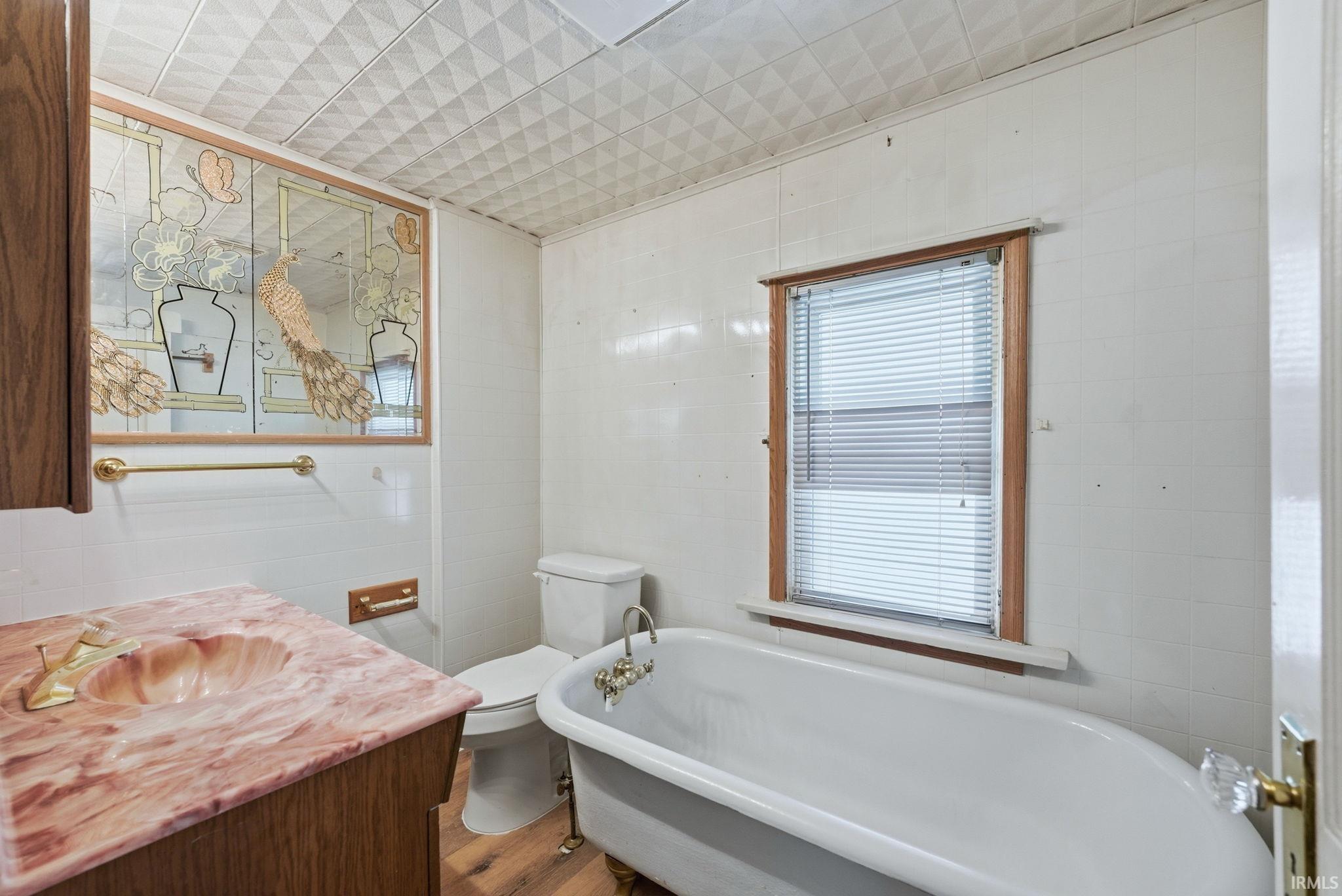 Vintage-style bathroom featuring a classic clawfoot tub, wood-finish flooring, and a unique vanity with a shell-shaped basin and pink marble-look countertop