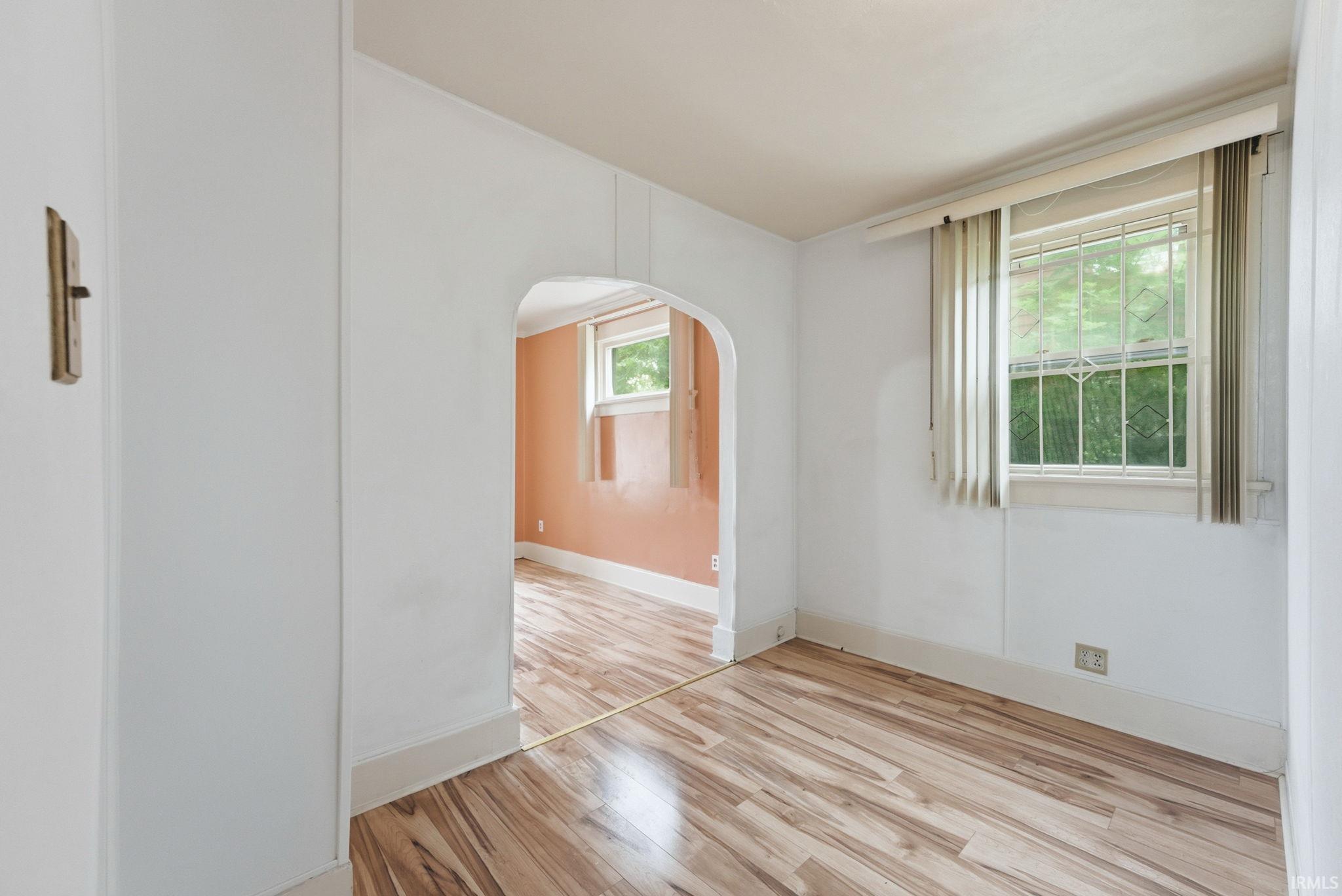 Bright room with wood-finish flooring, white baseboards, and a window with security bars