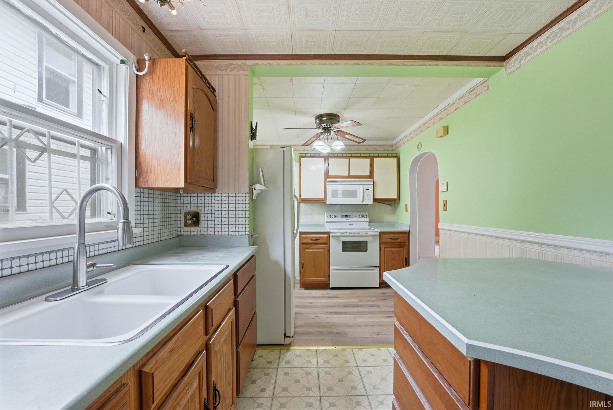 Kitchen featuring wood cabinetry, a double basin sink with a gooseneck faucet, light green countertops, and white appliances