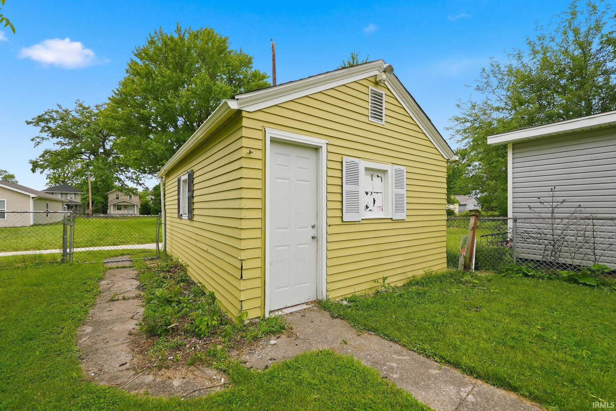 Detached accessory structure with yellow horizontal siding, a white entry door, and a gable roof
