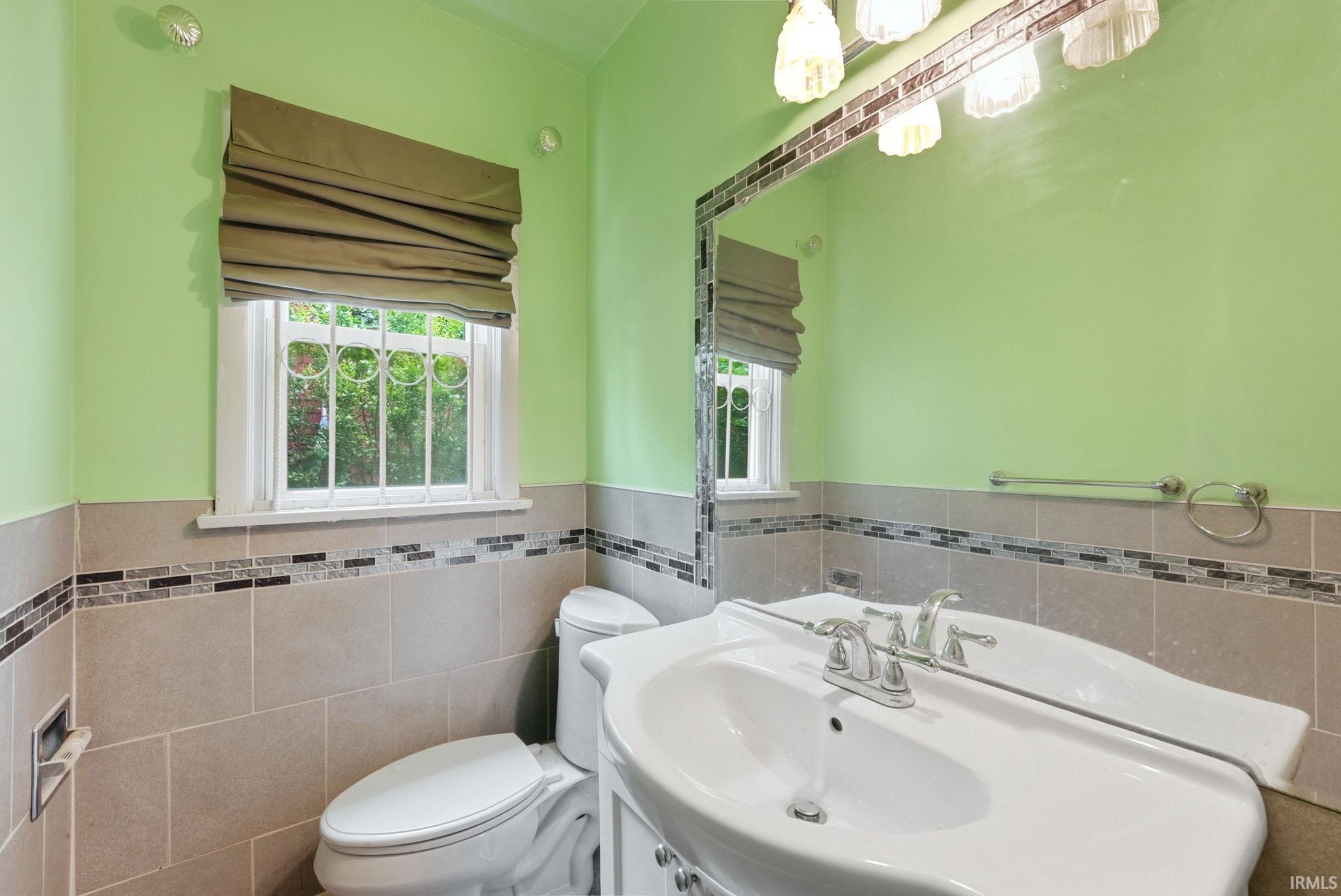 Bathroom featuring a white vanity with a single basin sink, a large mirror with mosaic tile trim, and sconce lighting