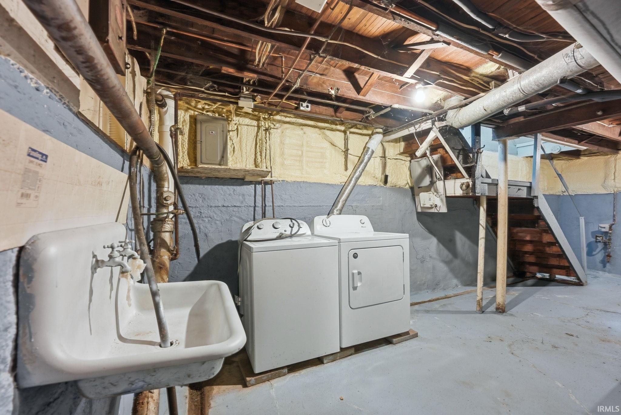 Utility area featuring a wall-mounted basin, washer and dryer, exposed ceiling joists, and a partial staircase