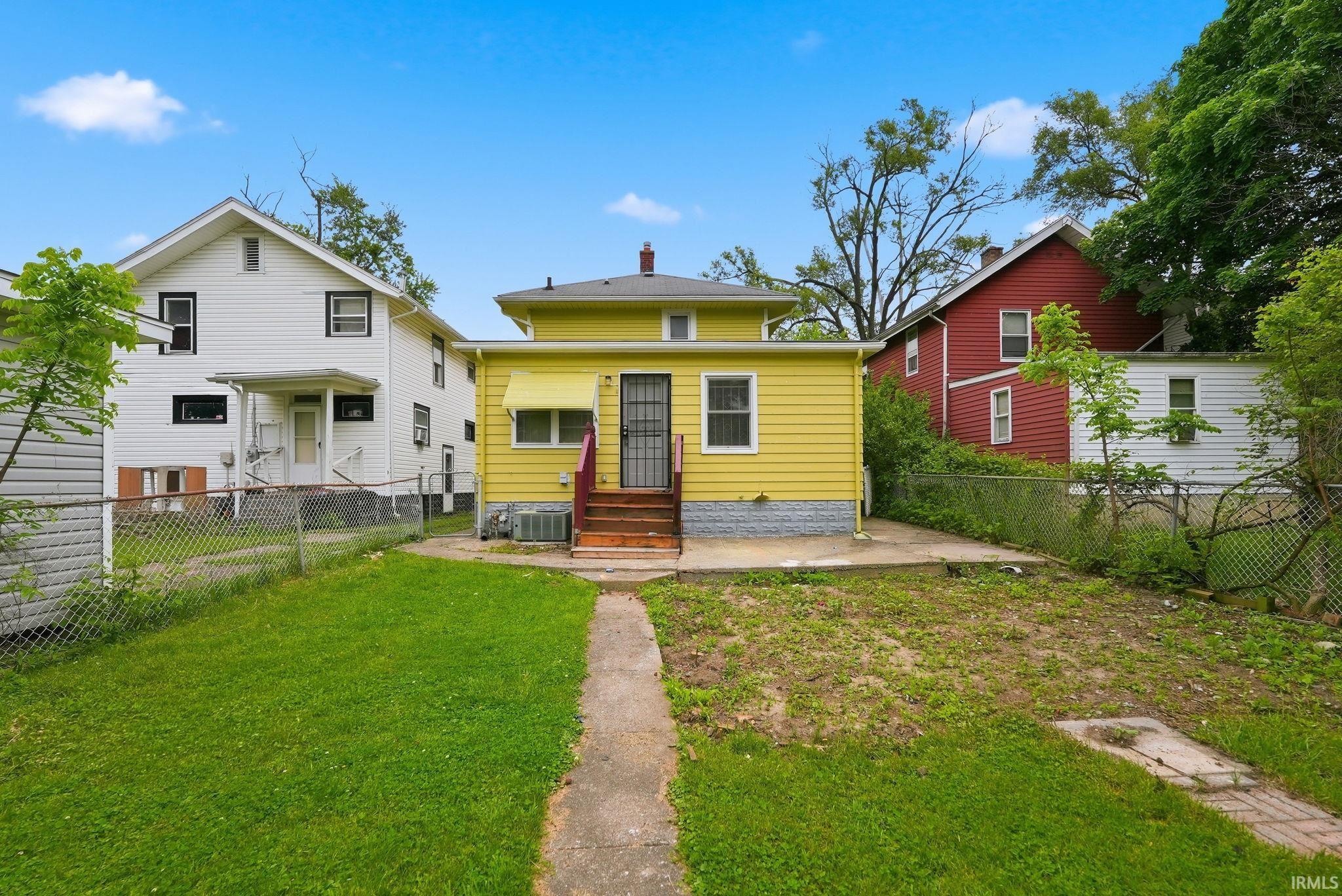 Yellow siding exterior with a concrete patio, wood steps, and a wrought iron security door