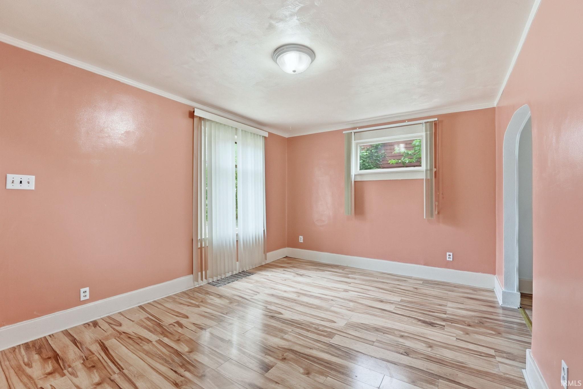 Room featuring wood-finish flooring, two windows with blinds, an arched doorway, and a flush-mount ceiling light