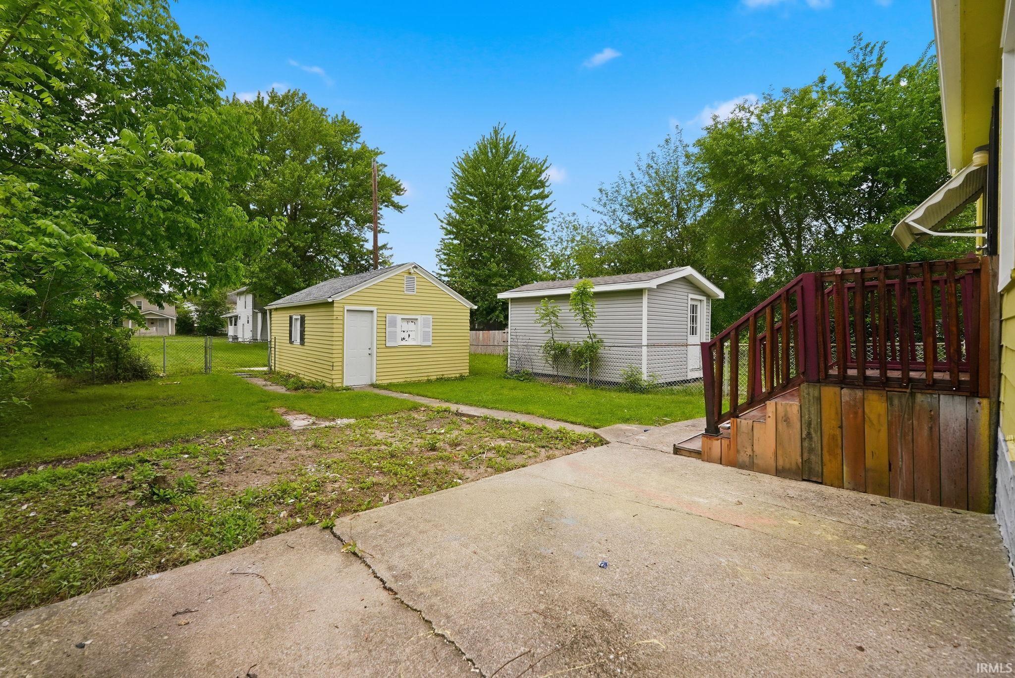 Expansive backyard featuring a concrete patio, a multi-tone wood deck with railing, and two detached storage sheds