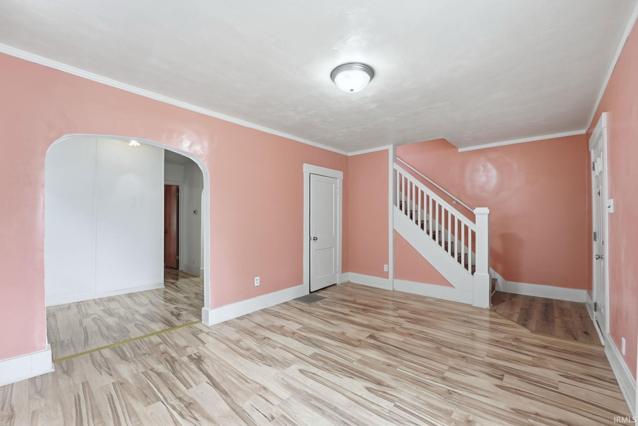 Open-concept interior featuring wood-finish flooring, a white staircase with balusters, and an arched doorway