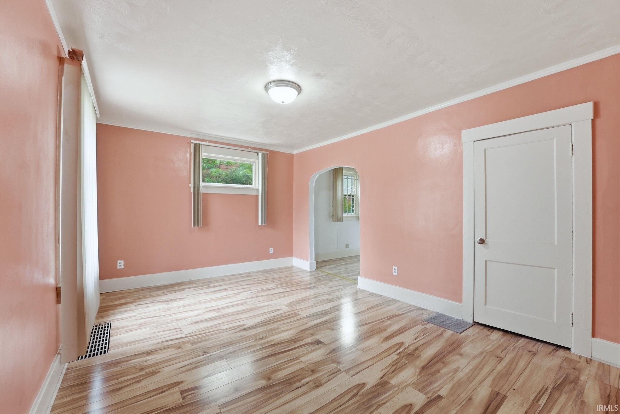 Spacious room featuring wood-finish flooring, an arched doorway, and a ceiling-mounted light fixture