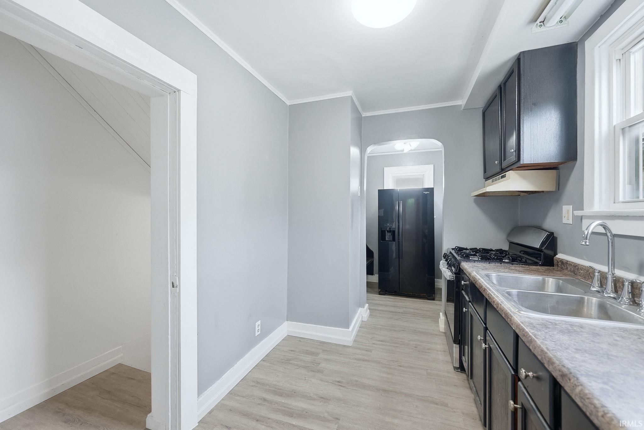 Galley kitchen featuring wood-finish flooring, dark cabinetry, and a double basin stainless steel sink with a gooseneck faucet