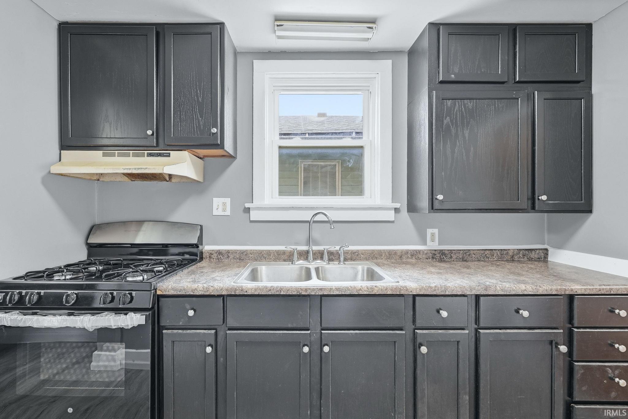Kitchen featuring dark cabinetry, laminate countertops, a double basin stainless steel sink, and a four-burner gas range with oven
