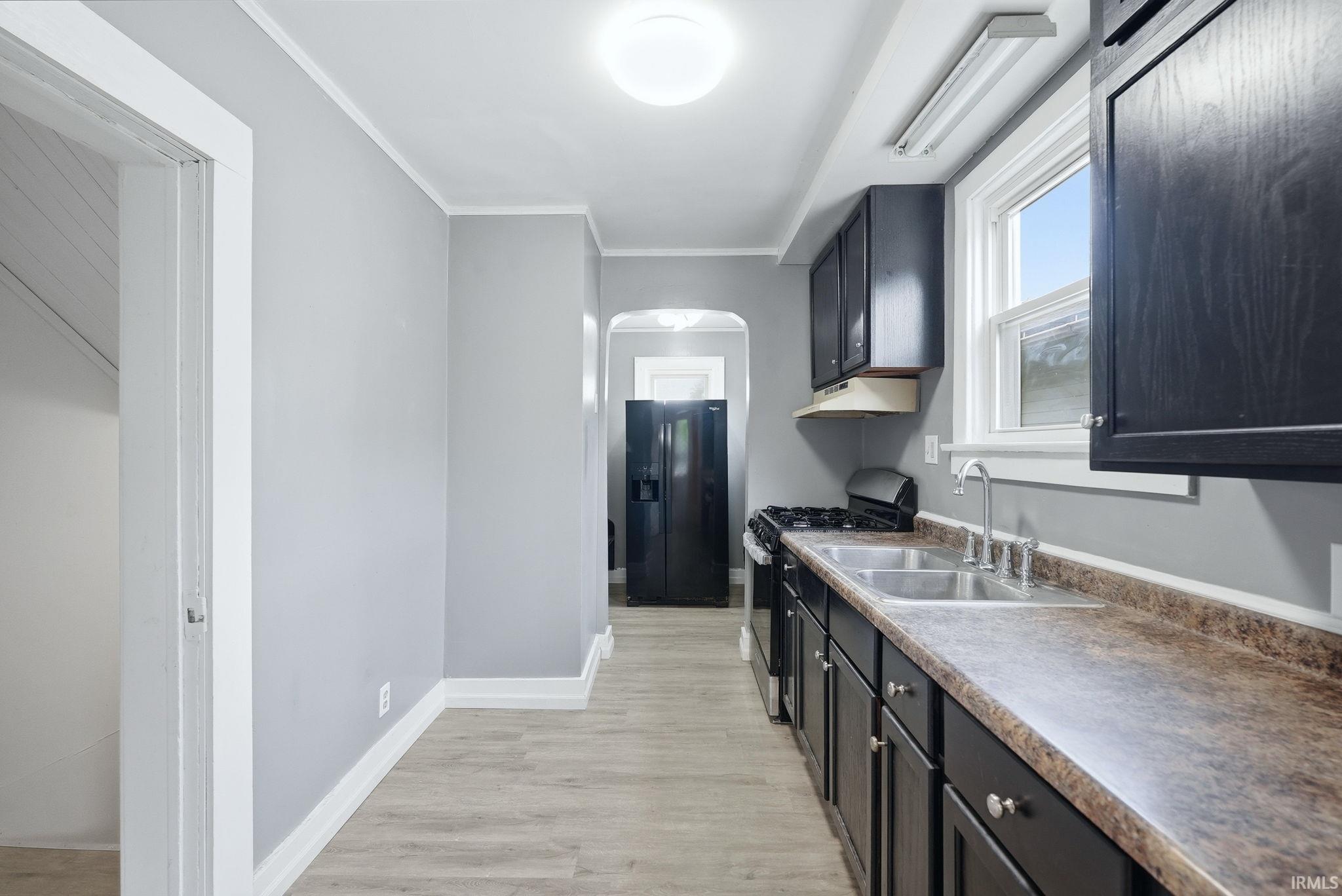 Galley kitchen featuring wood-finish flooring, dark wood cabinetry, a double basin stainless steel sink, and light gray painted walls
