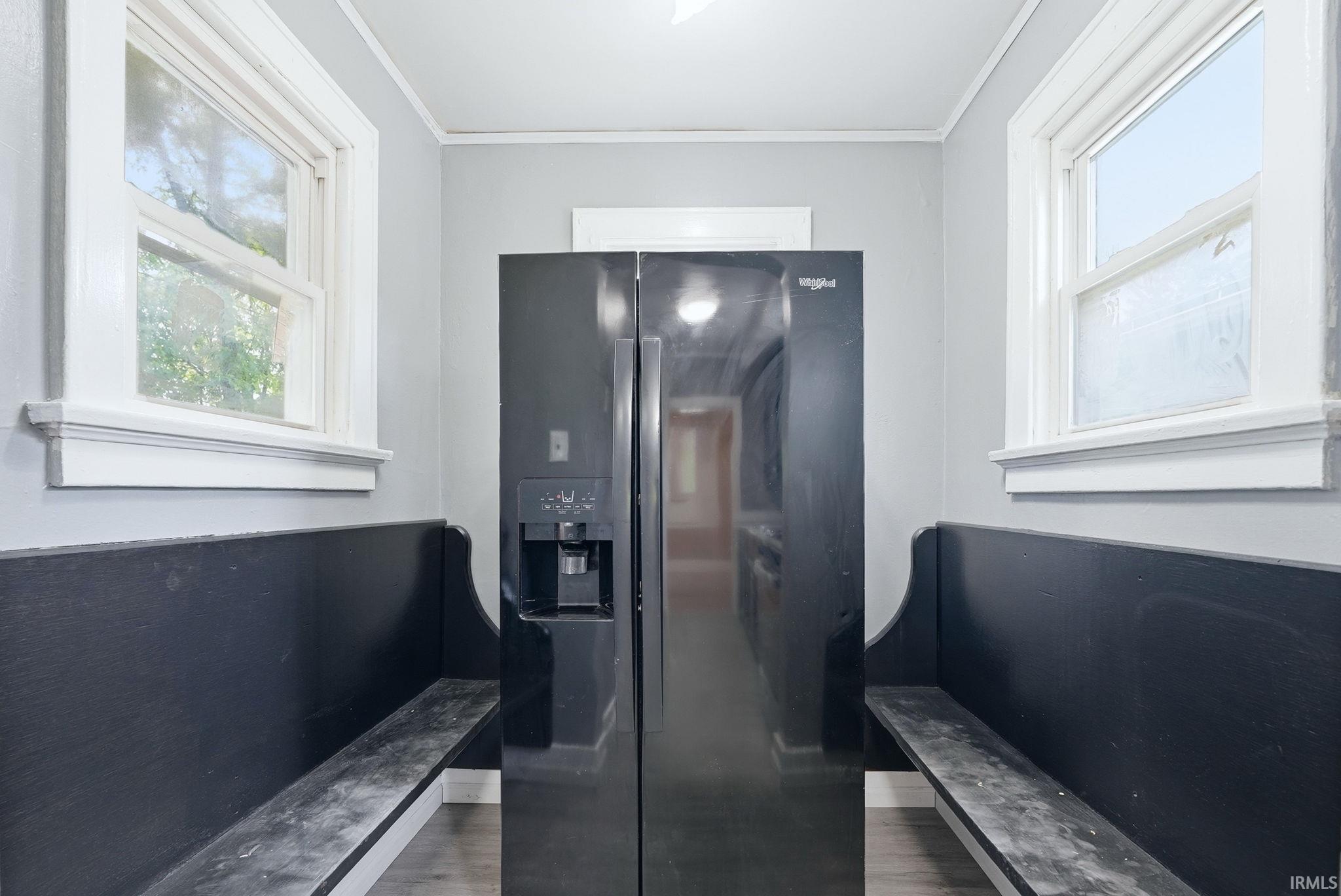 Recessed black side-by-side refrigerator, flanked by two built-in black benches with storage, set against light gray walls with white trim and wood-finish flooring
