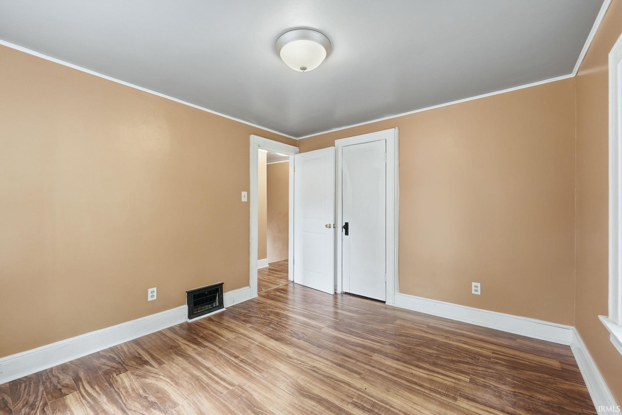 Spacious interior room featuring wood-finish flooring, light tan walls, and white trim