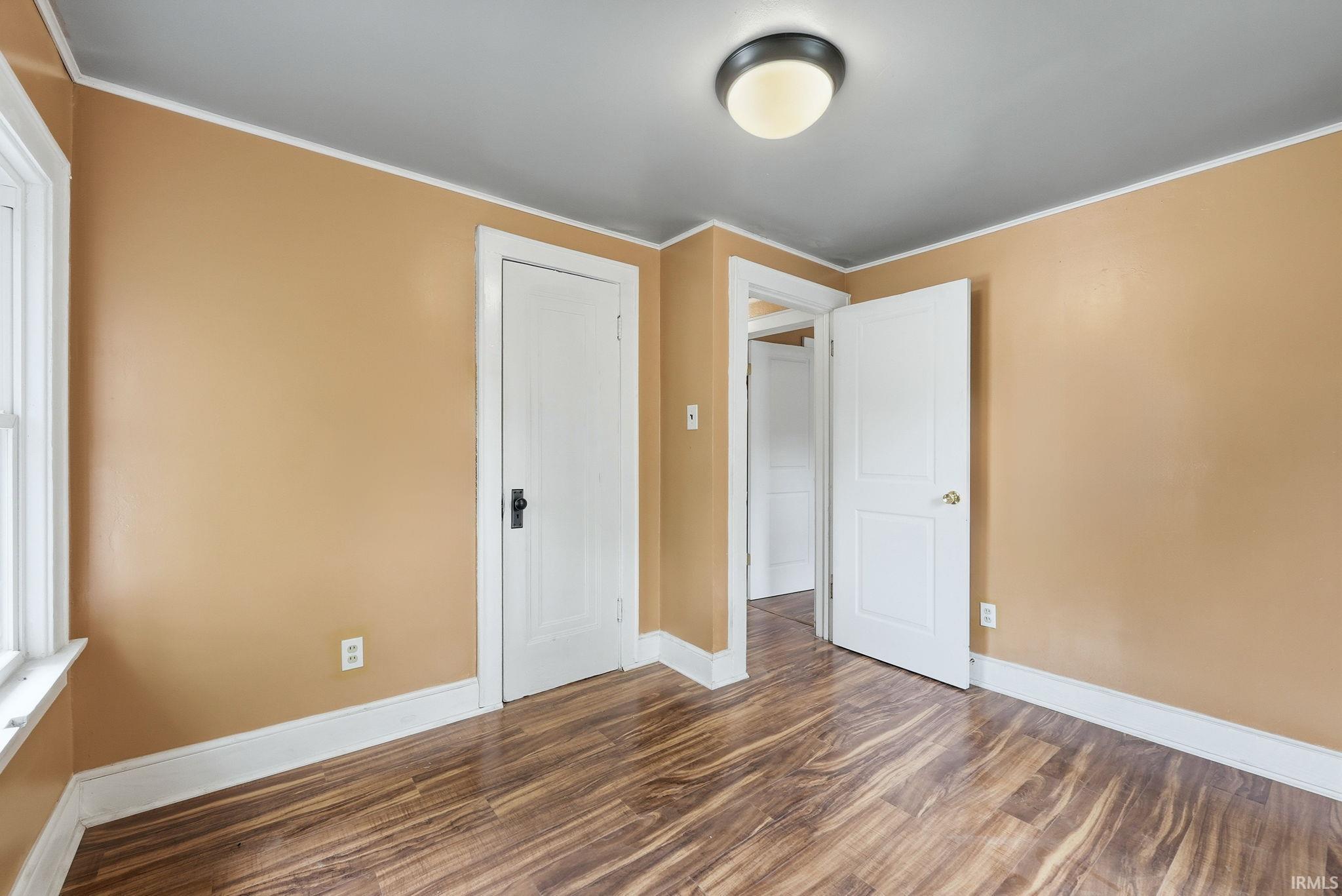 Room featuring wood-finish flooring, light tan walls, and white trim