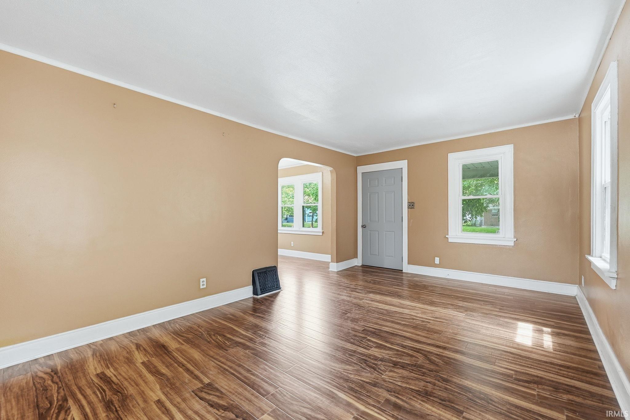 Spacious room featuring wood-finish flooring, light tan walls, white trim, and multiple windows providing natural light