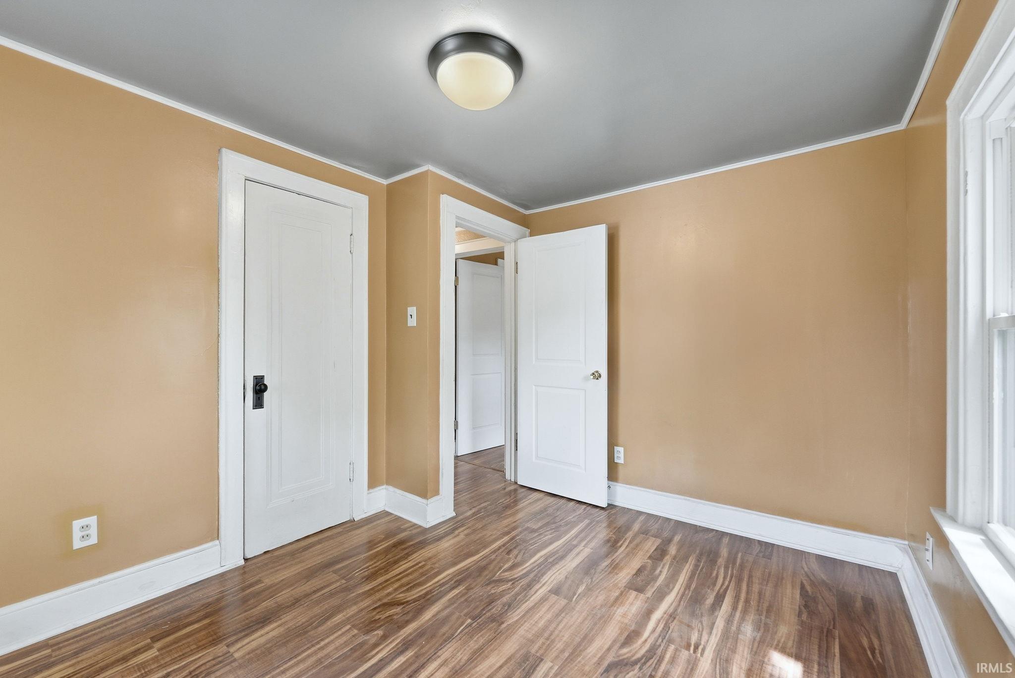Neutral-toned room featuring rich wood-finish flooring, white trim, a flush mount ceiling light fixture, and a white paneled door with a dark handle