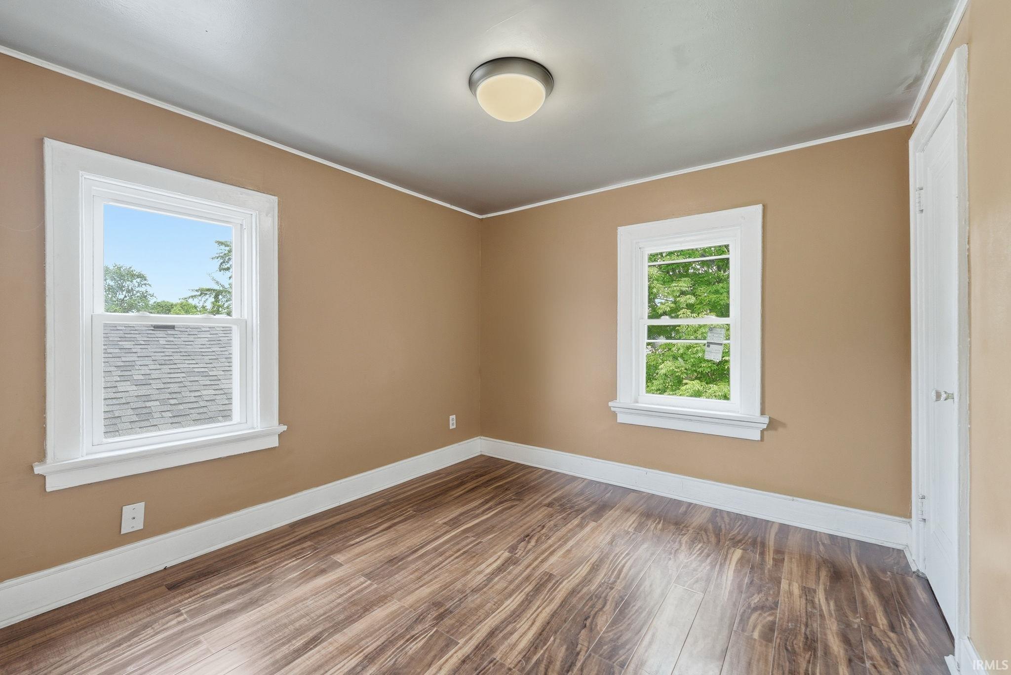 Room featuring wood-finish flooring, two windows with white trim, and a ceiling-mounted light fixture