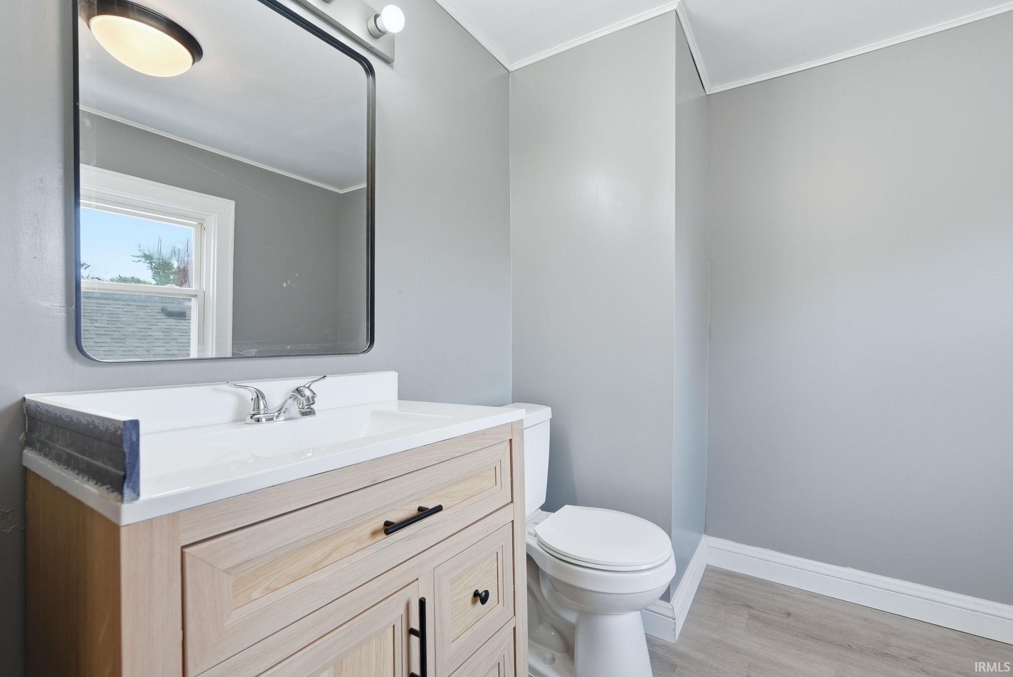 Modern bathroom featuring light gray walls, wood-finish vanity with black hardware, white countertop with integrated sink, and a sleek rectangular mirror