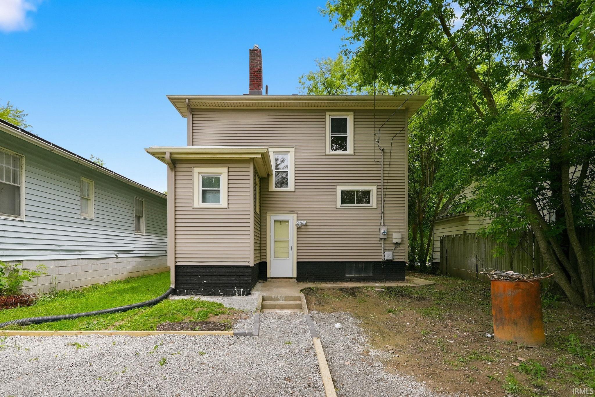 Rear exterior featuring horizontal siding, white trim windows, a white entry door, and a brick chimney