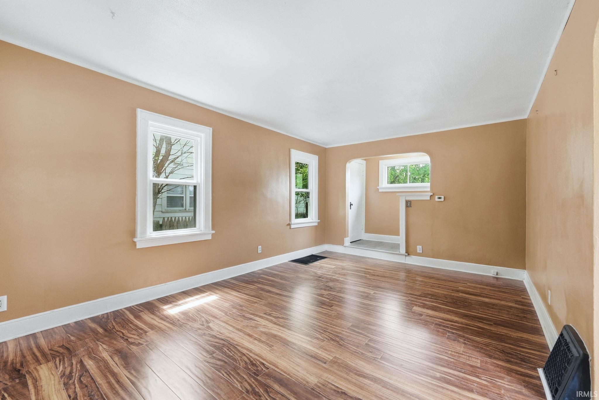 Spacious interior featuring wood-finish flooring, multiple windows with white trim, and an arched entryway