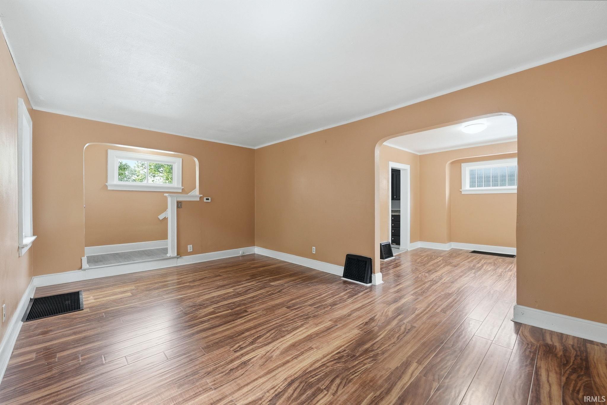 Spacious interior room featuring wood-finish flooring, light tan walls, white trim, and an arched doorway