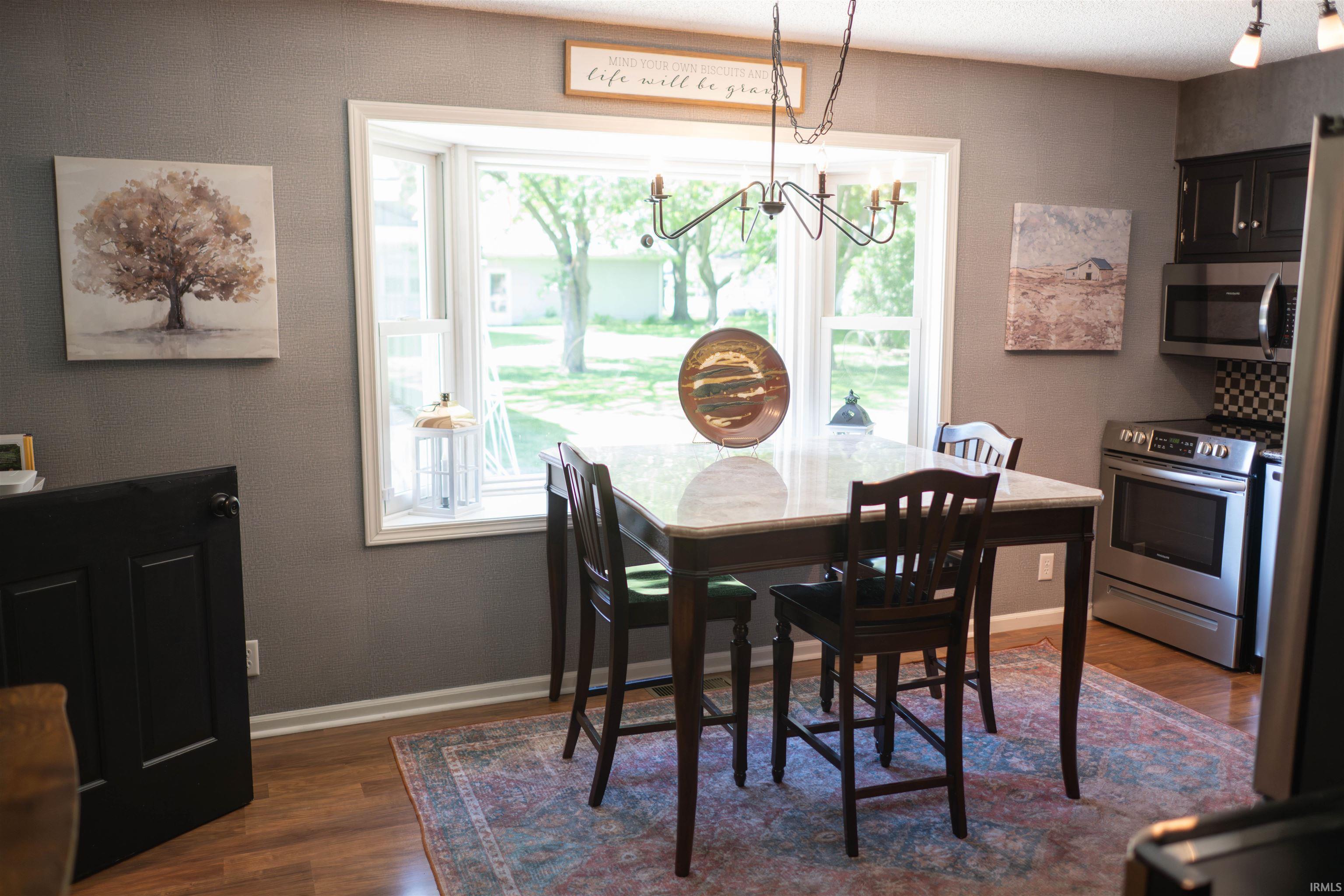 Bay window with white trim, wood-finish flooring, and a chandelier-style fixture