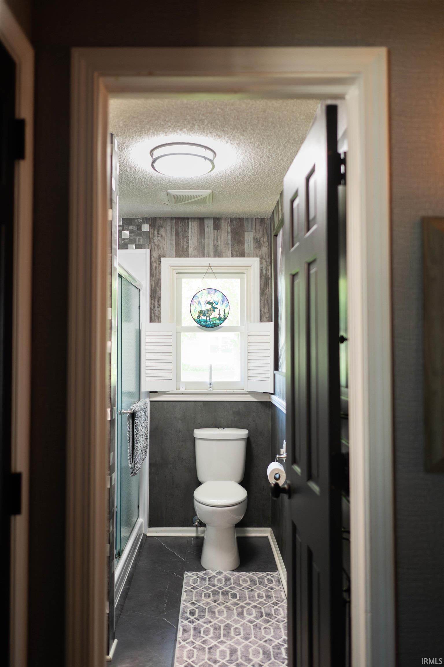 Bathroom featuring a glass-enclosed shower, dark slate-style flooring, and a window with white louvered shutters