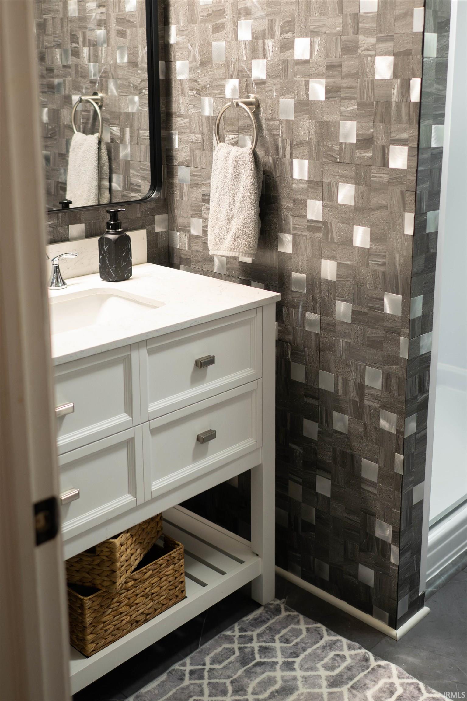 Contemporary bathroom featuring a white vanity with integrated sink, modern faucet, and a wall of square mosaic tiles