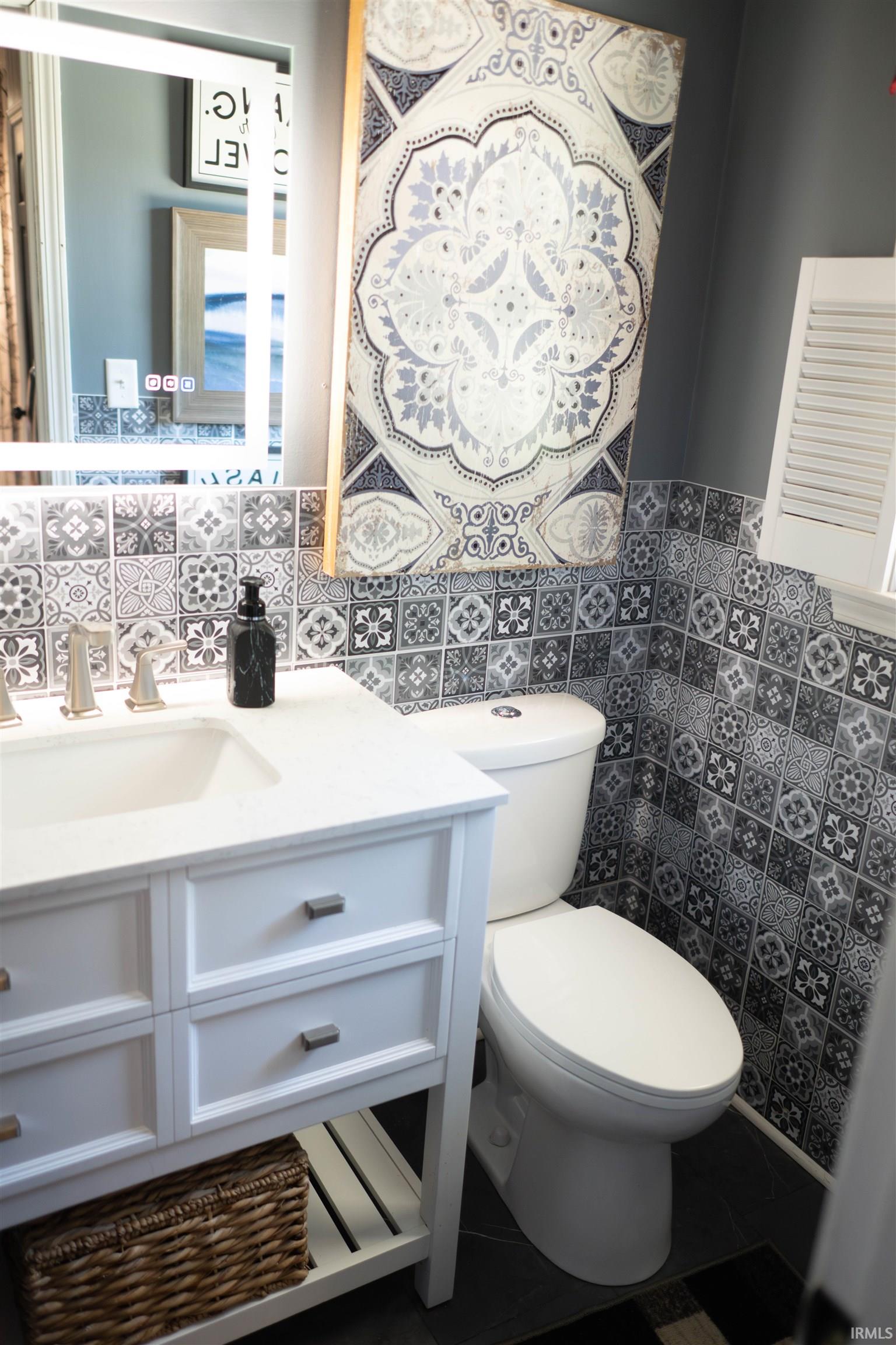 Bathroom featuring a white vanity with an integrated sink, patterned wall tile, and a backlit mirror