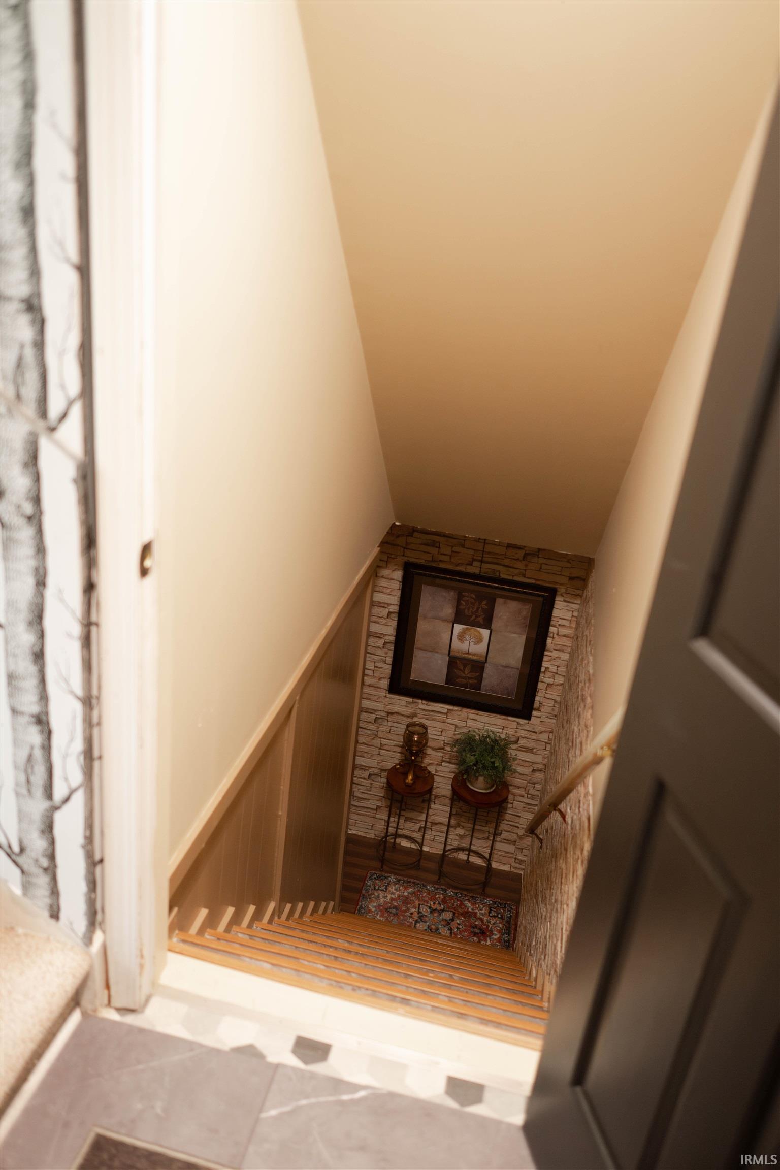 Staircase featuring wood-finish treads, a wood-finish handrail, and stone-look wall paneling