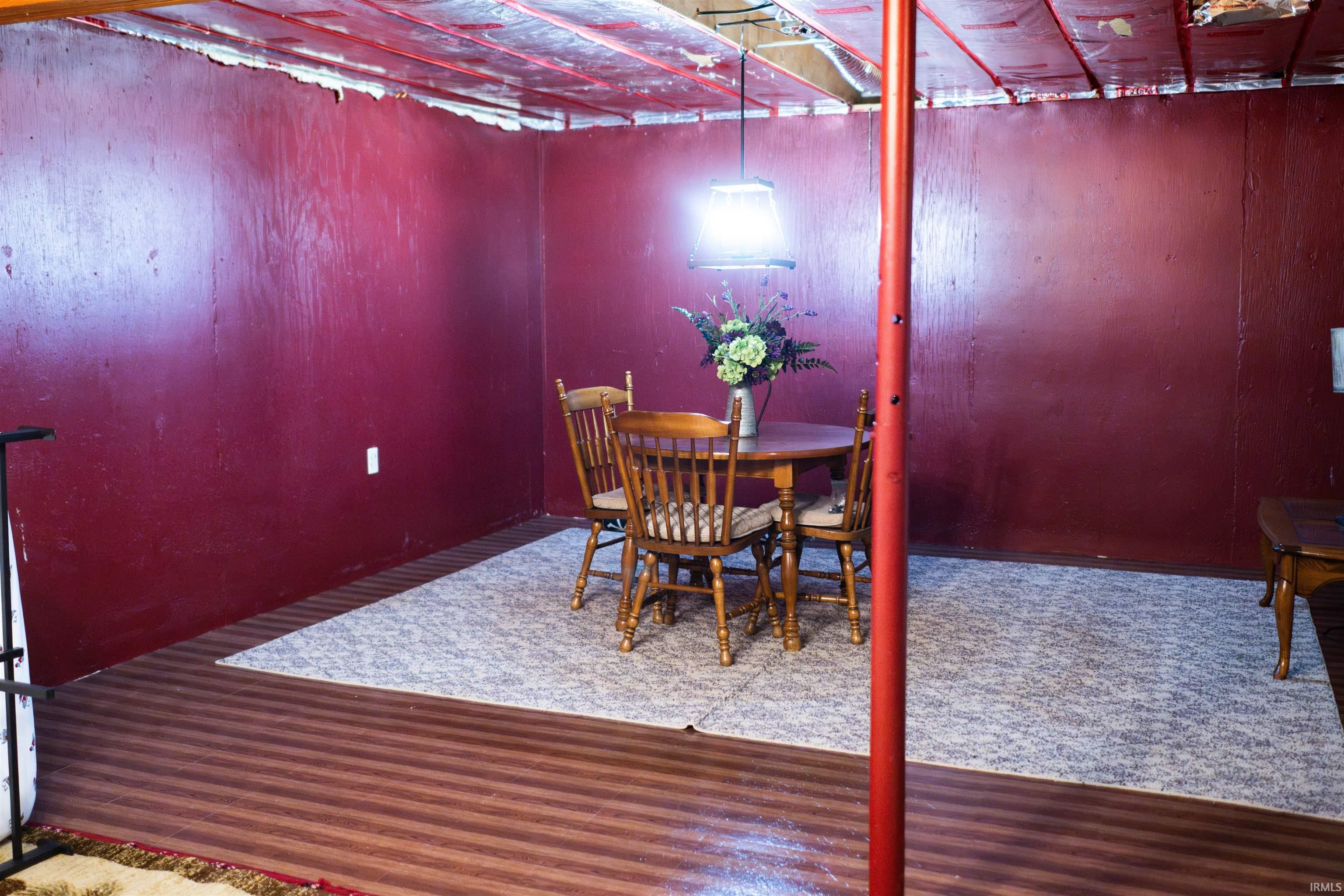 Finished room featuring wood-finish flooring with a light-colored area rug, bold red walls, and an exposed ceiling