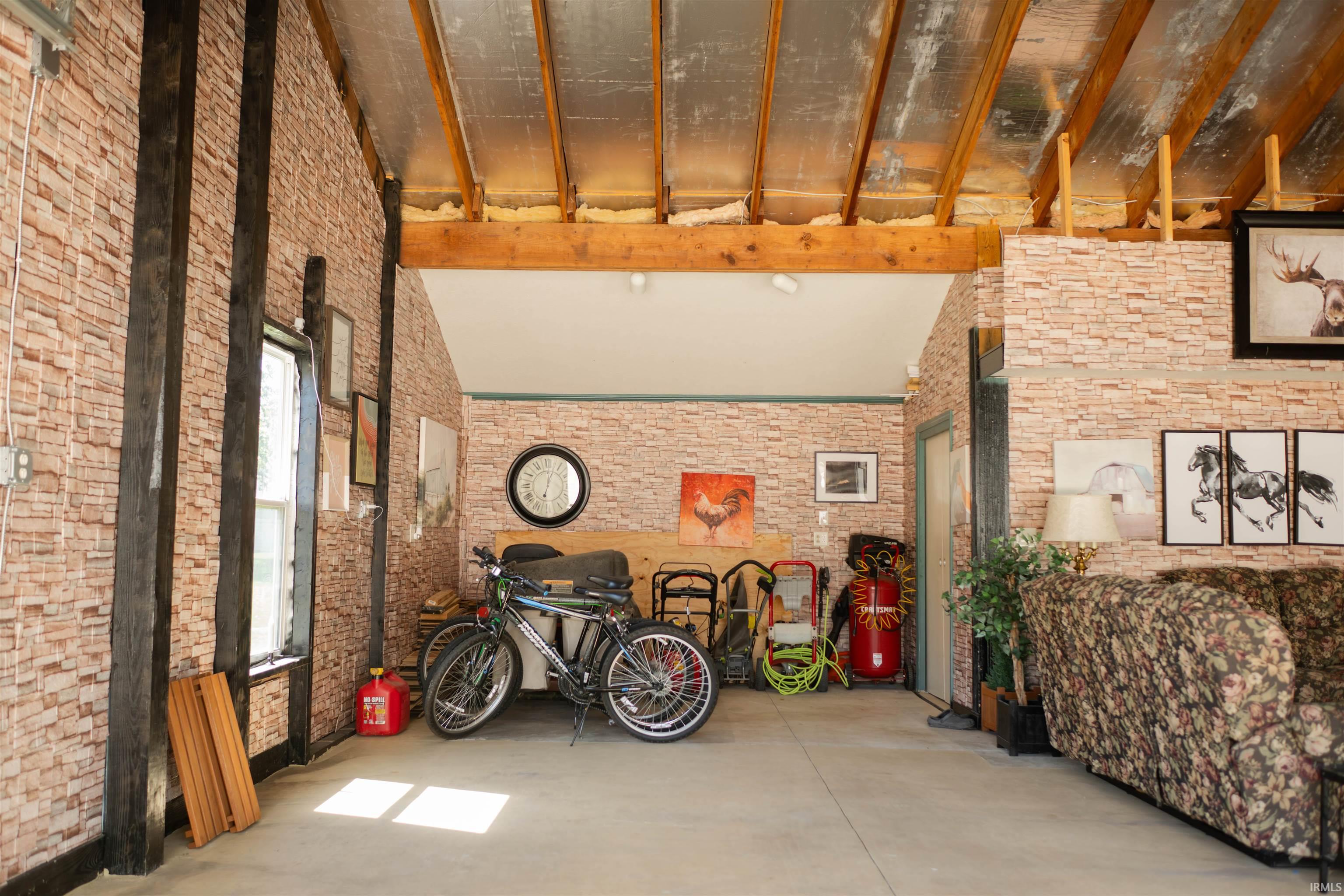 Spacious interior featuring exposed wooden beams, brick-patterned wall finishes, a vaulted ceiling, and a light-colored concrete floor