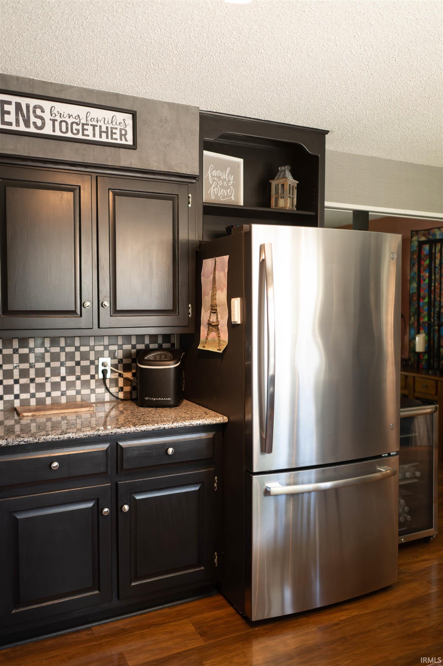 Kitchen featuring black cabinetry, speckled countertops, a mosaic tile backsplash, and stainless steel appliances