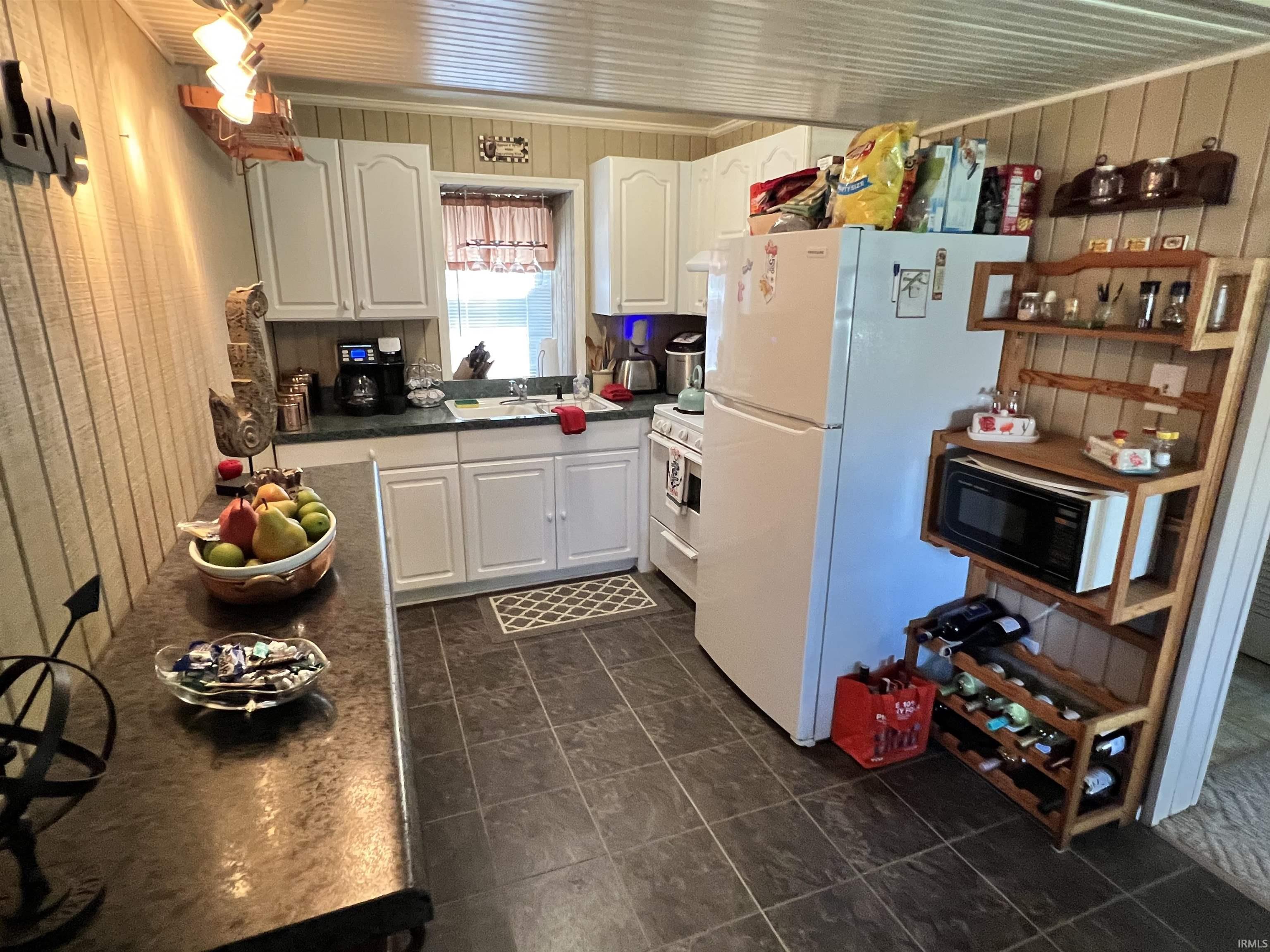 Efficient kitchen featuring white cabinetry, dark countertop surfaces, a window above the sink, and tile flooring
