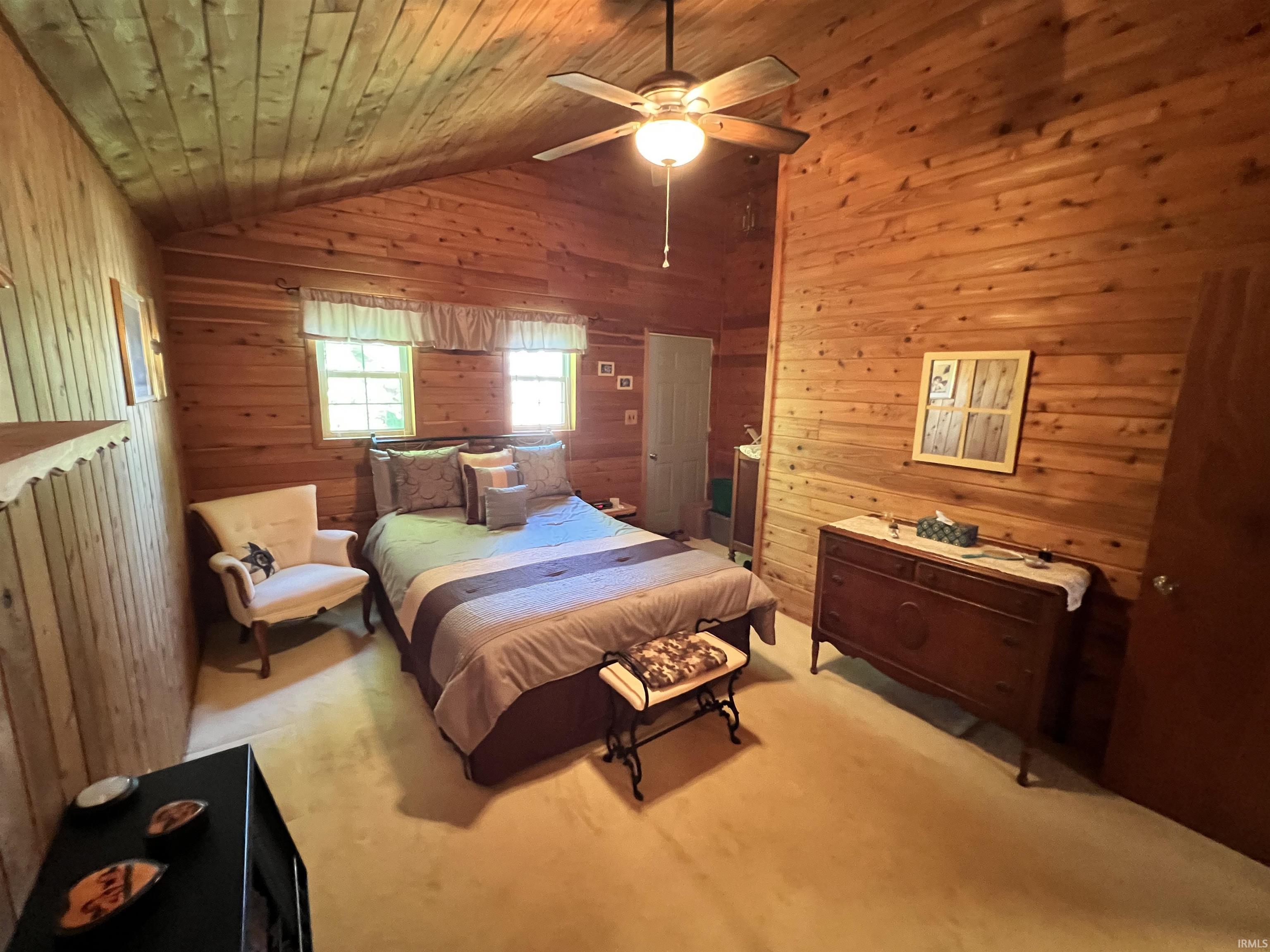 Room featuring wood paneling on walls and vaulted ceiling, ceiling fan with integrated lighting, and carpeted flooring