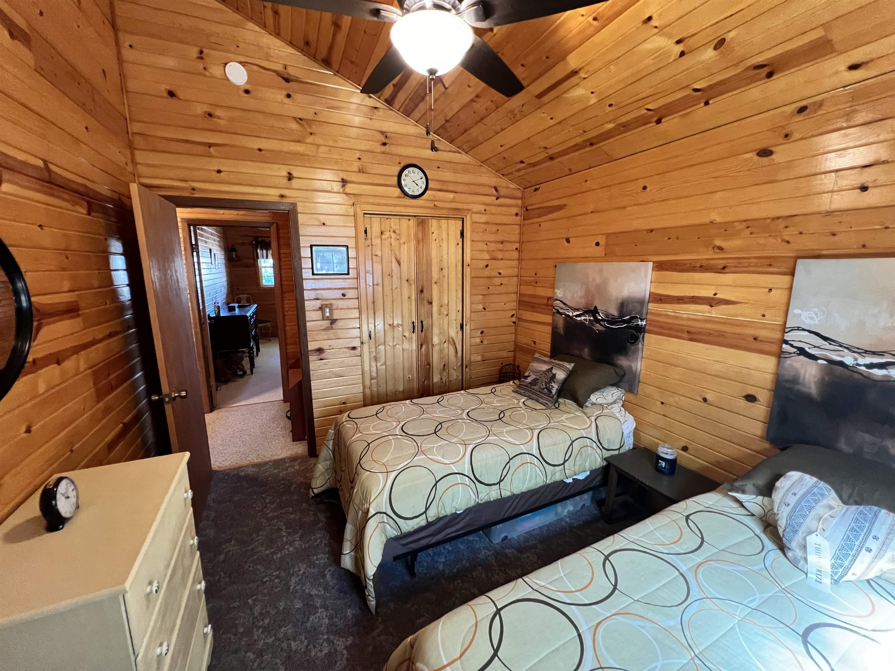 Vaulted ceiling with wood paneling, wood-paneled walls, ceiling fan with integrated lighting, wood-finish flooring, and a solid wood door